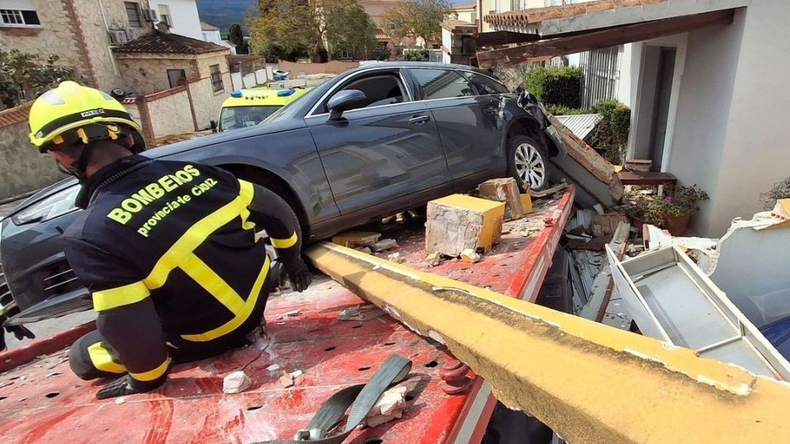 La grúa cargada con un coche, empotrada en una vivienda en Los Barrios.