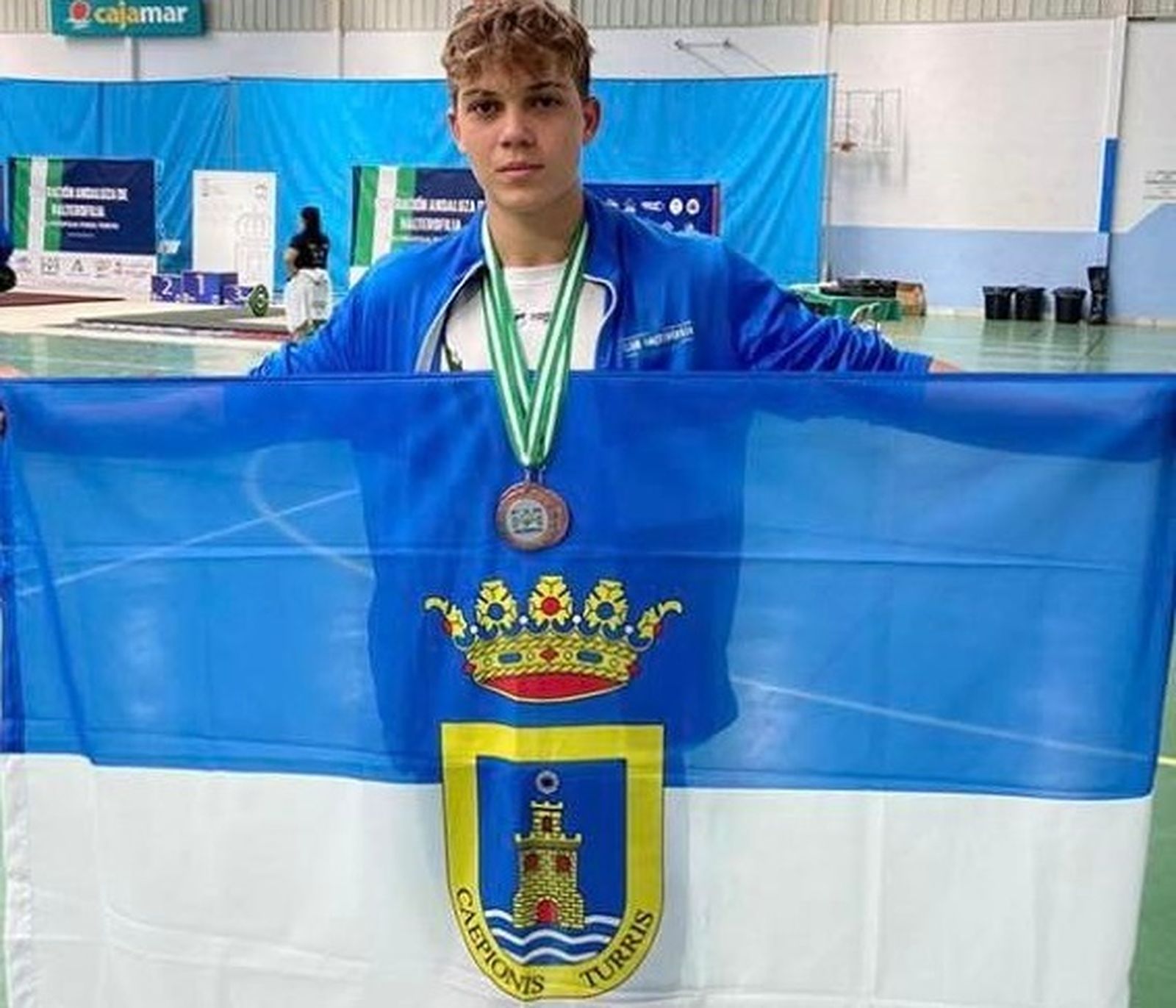 Chamorro posa con sus medallas mientras sostiene una bandera de Chipiona.