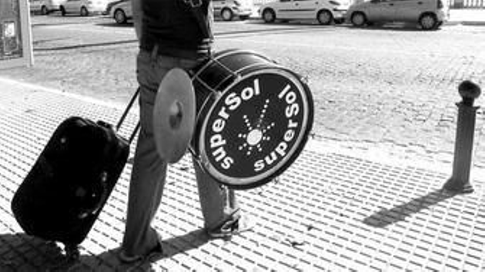 Un carnavalero, con el bombo de Supersol, espera el autobús que le lleva a cantar fuera de Cádiz.