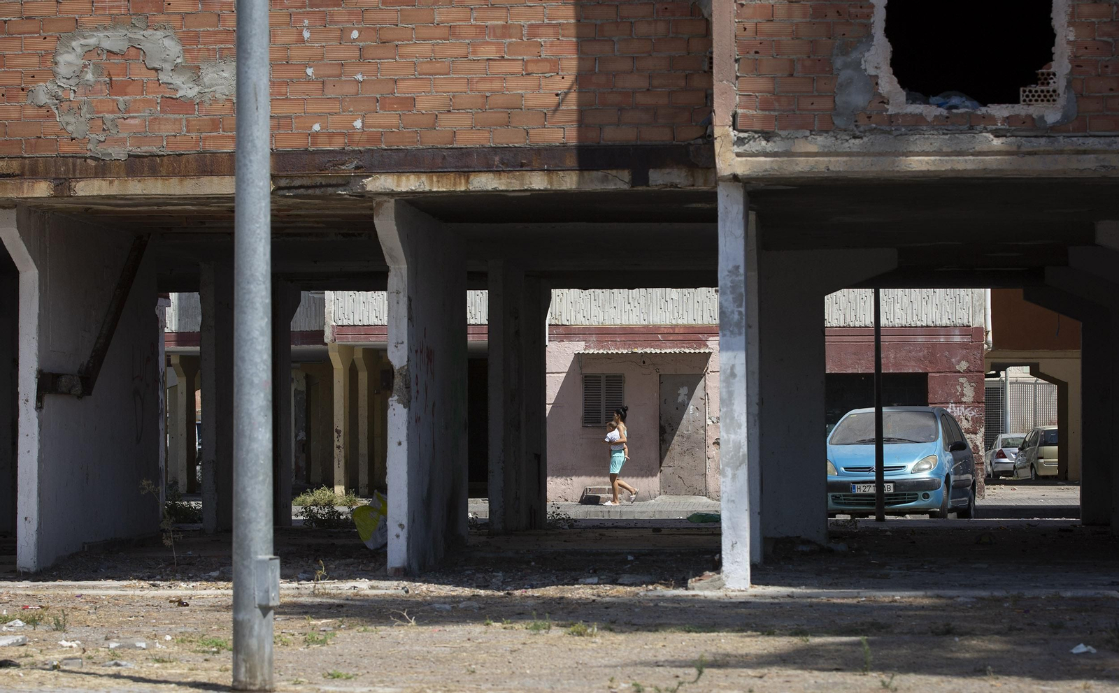 Una mujer con su hijo en brazos pasa entre unos bloques del Polígono Sur.