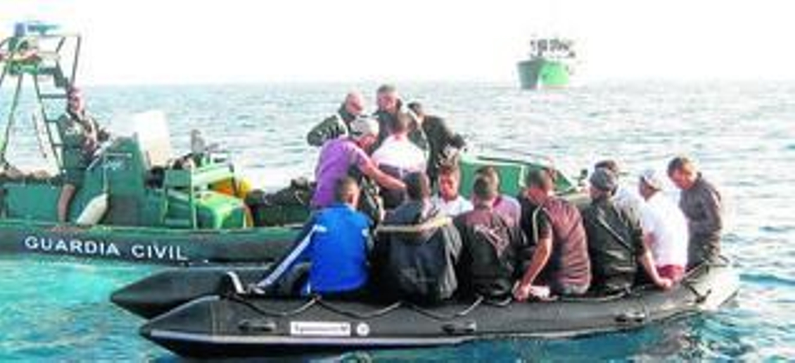 Momento en el que la tripulación del 'Río Miño', al fondo, desde una lancha fletada rescata a los inmigrantes.
