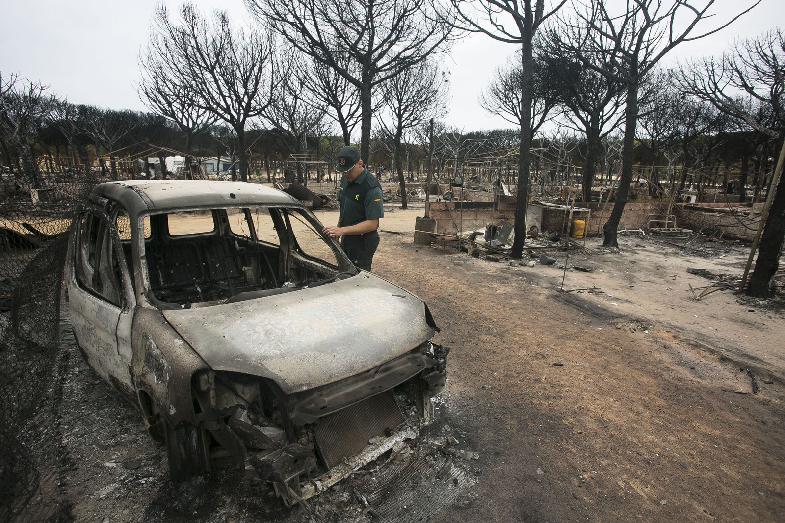 Un Guardia Civil ojea un vehículo calcinado en el Camping Doñana tras el incendio del pasado verano.