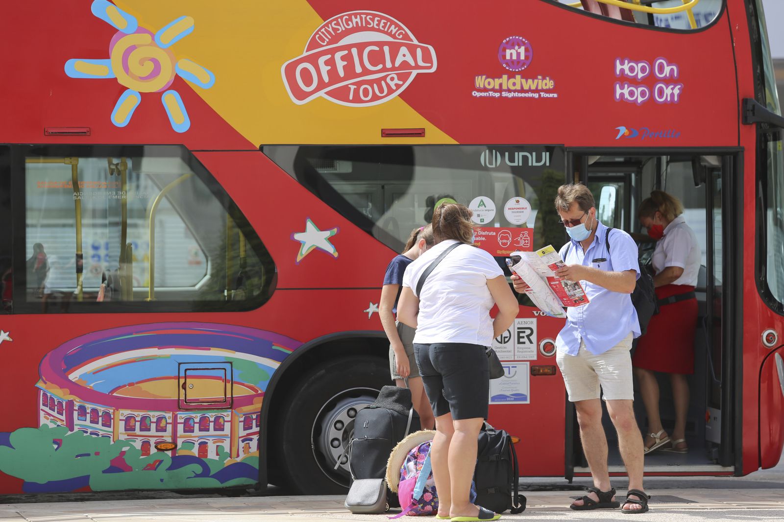 Unos turistas miran un mapa junto al autobús turístico de Málaga capital.