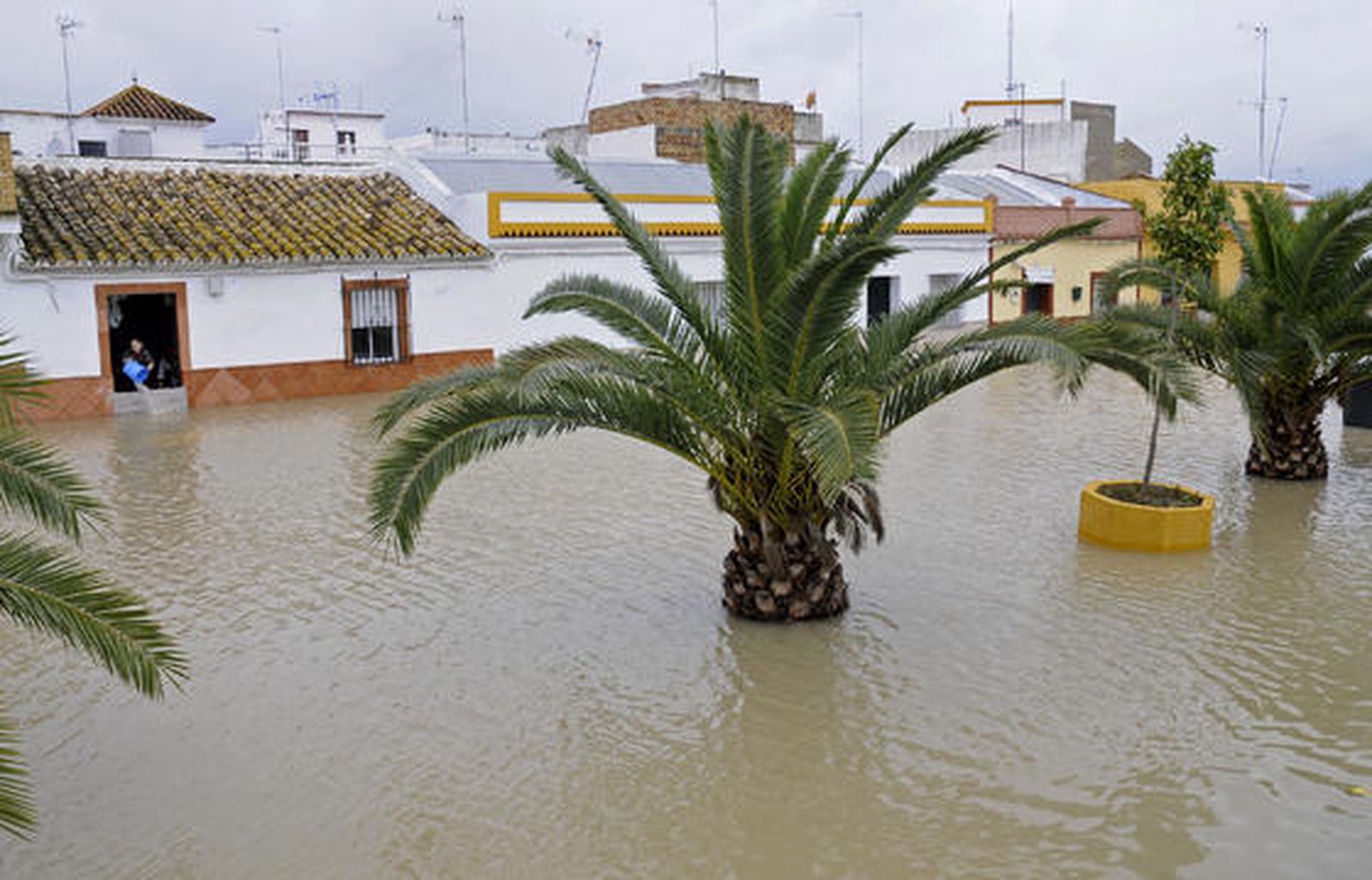 Una calle de Tocina inundada; al fondo, una mujer achicando agua.

Foto: Juan Carlos Vázquez