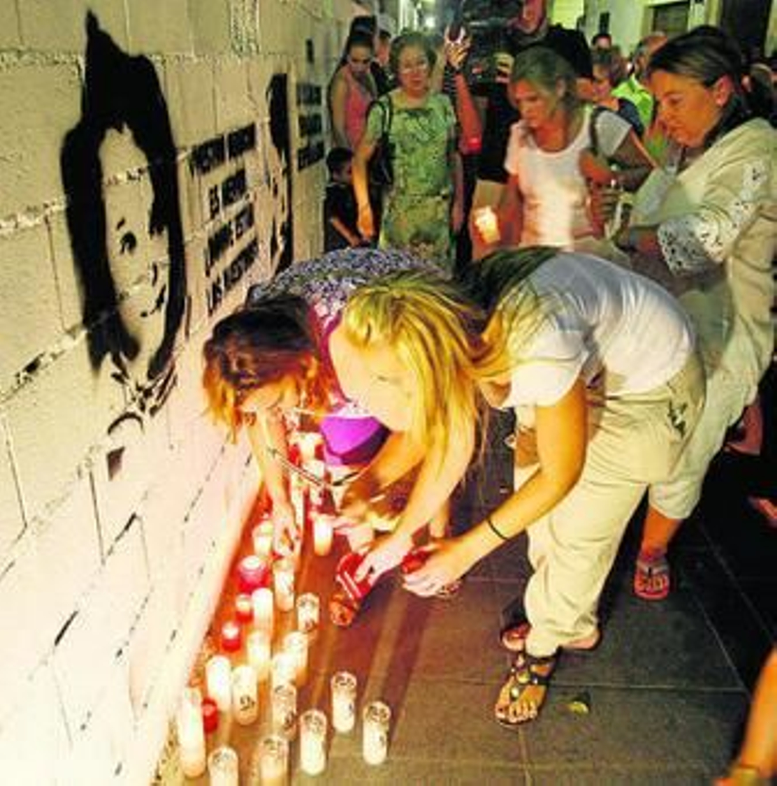 Varias personas ponen velas junto a la imagen de los niños.