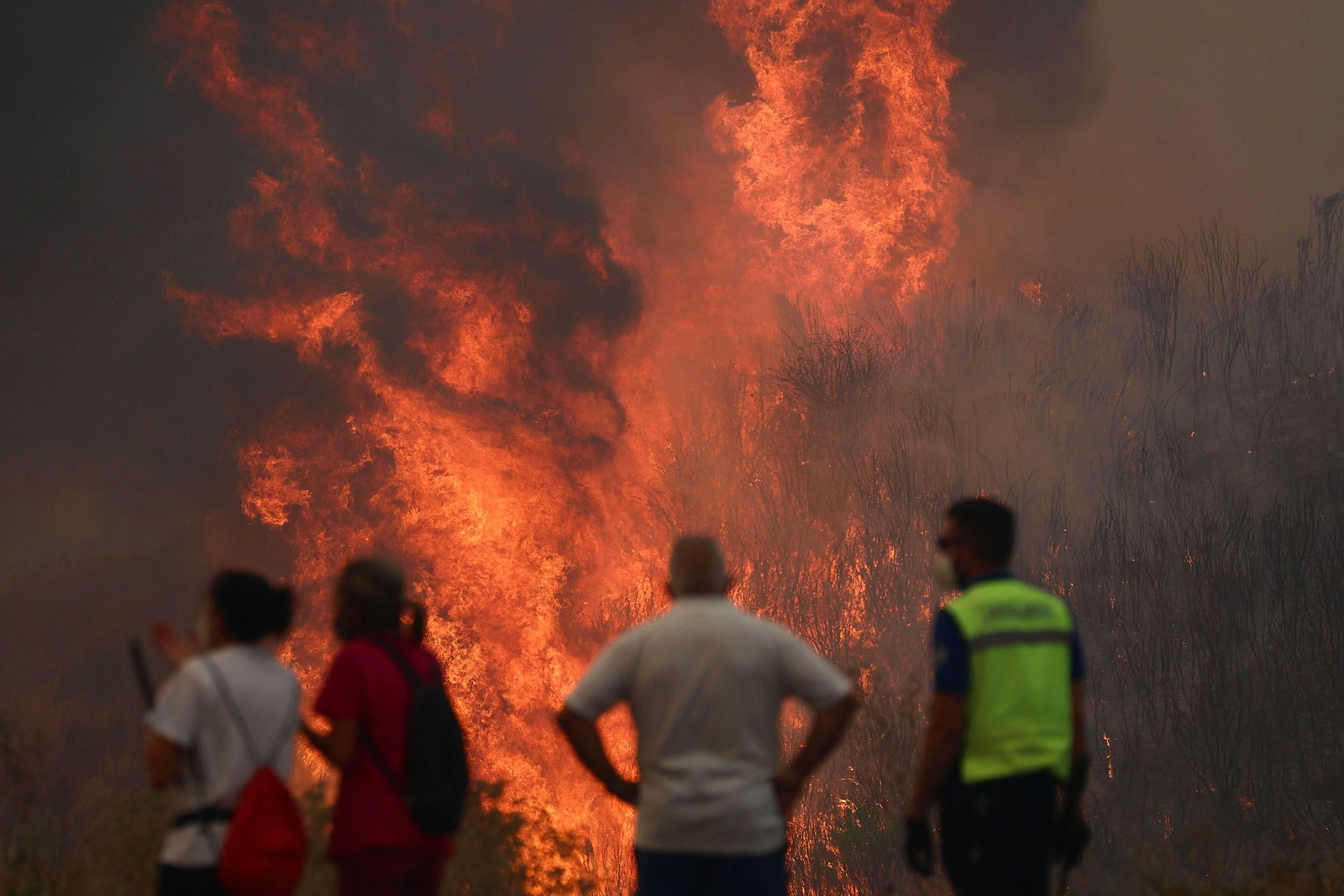 Varias personas observan las llamas descontroladas en un incendio en Galicia.