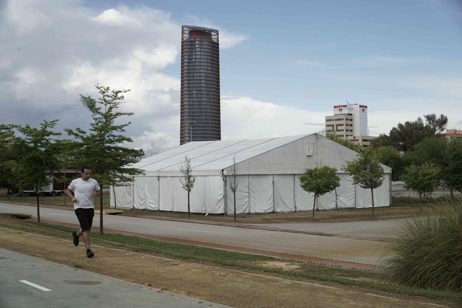 Un corredor pasa junto a una de las carpas instaladas el pasado abril en el Parque Vega de Triana, con el rascacielos al fondo.