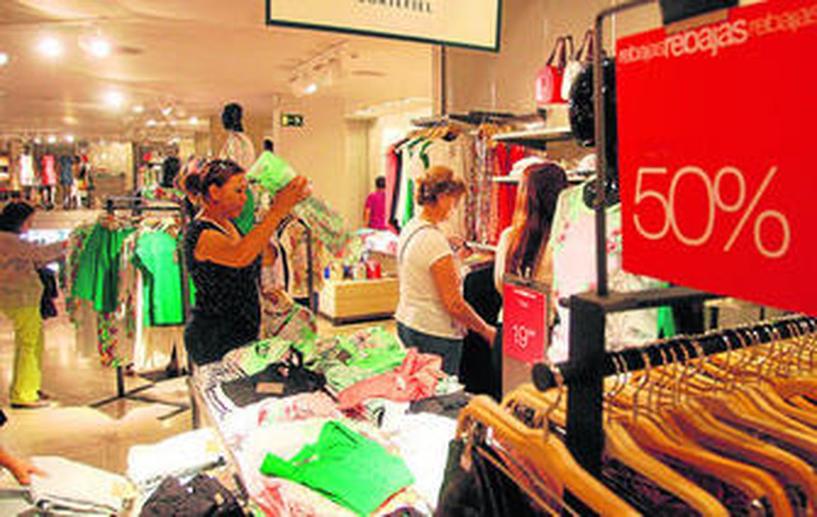 Varias personas miran mercancía en un establecimiento onubense durante el primer día oficial de las rebajas de verano.