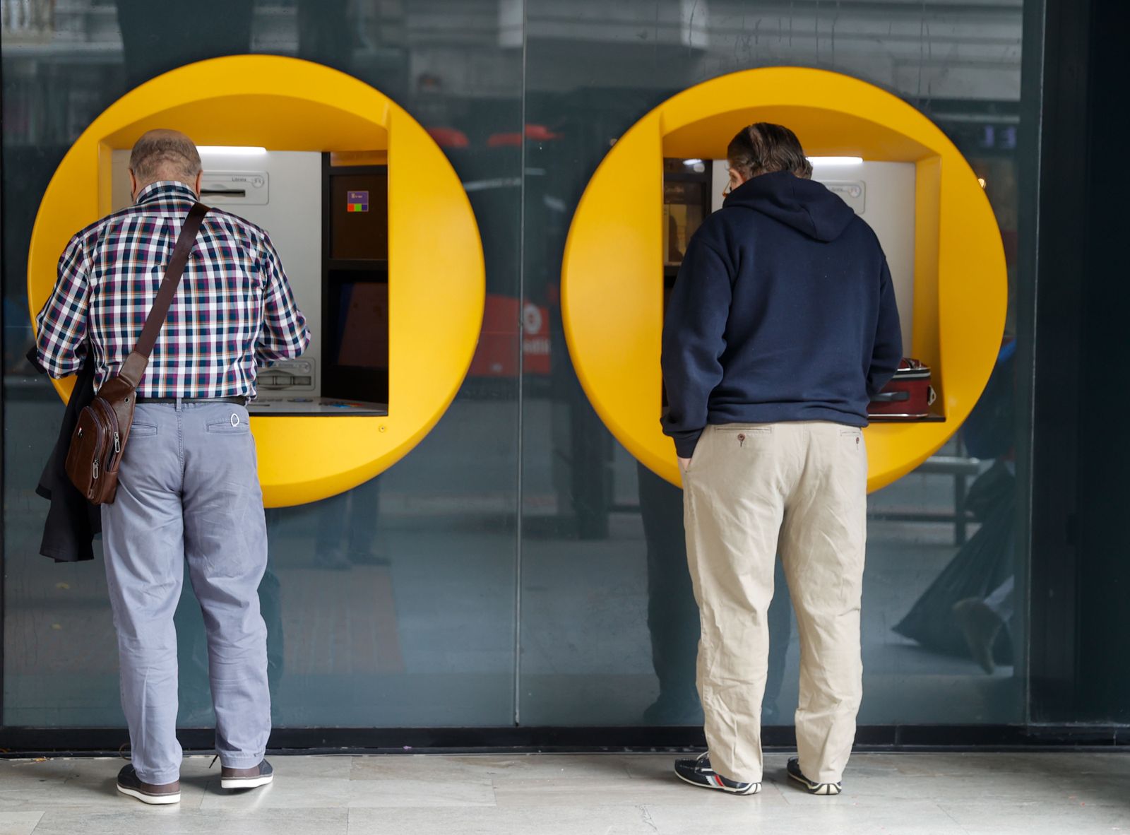 Dos personas sacan dinero de una entidad bancaria.