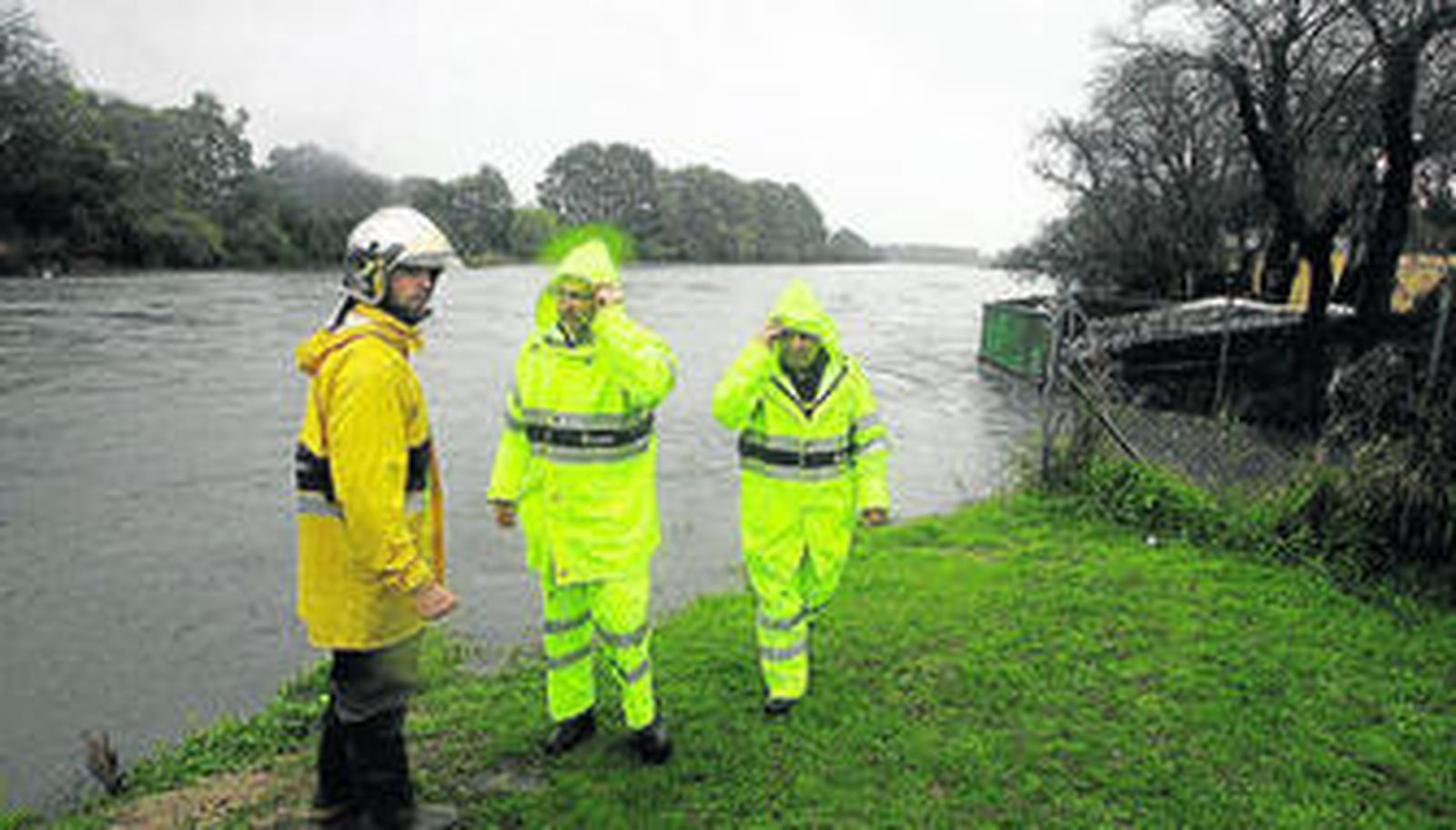 Tres miembros del cuerpo de Bomberos observan la crecida del río Guadarranque.