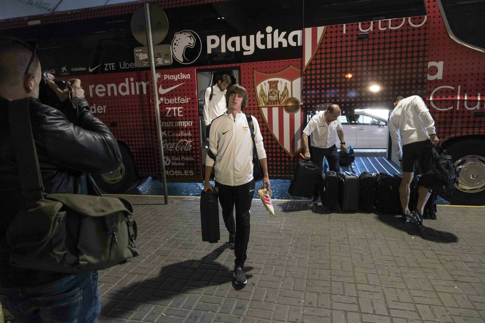 Bryan Gil, saliendo del autobús oficial del Sevilla con sus botas en la mano.