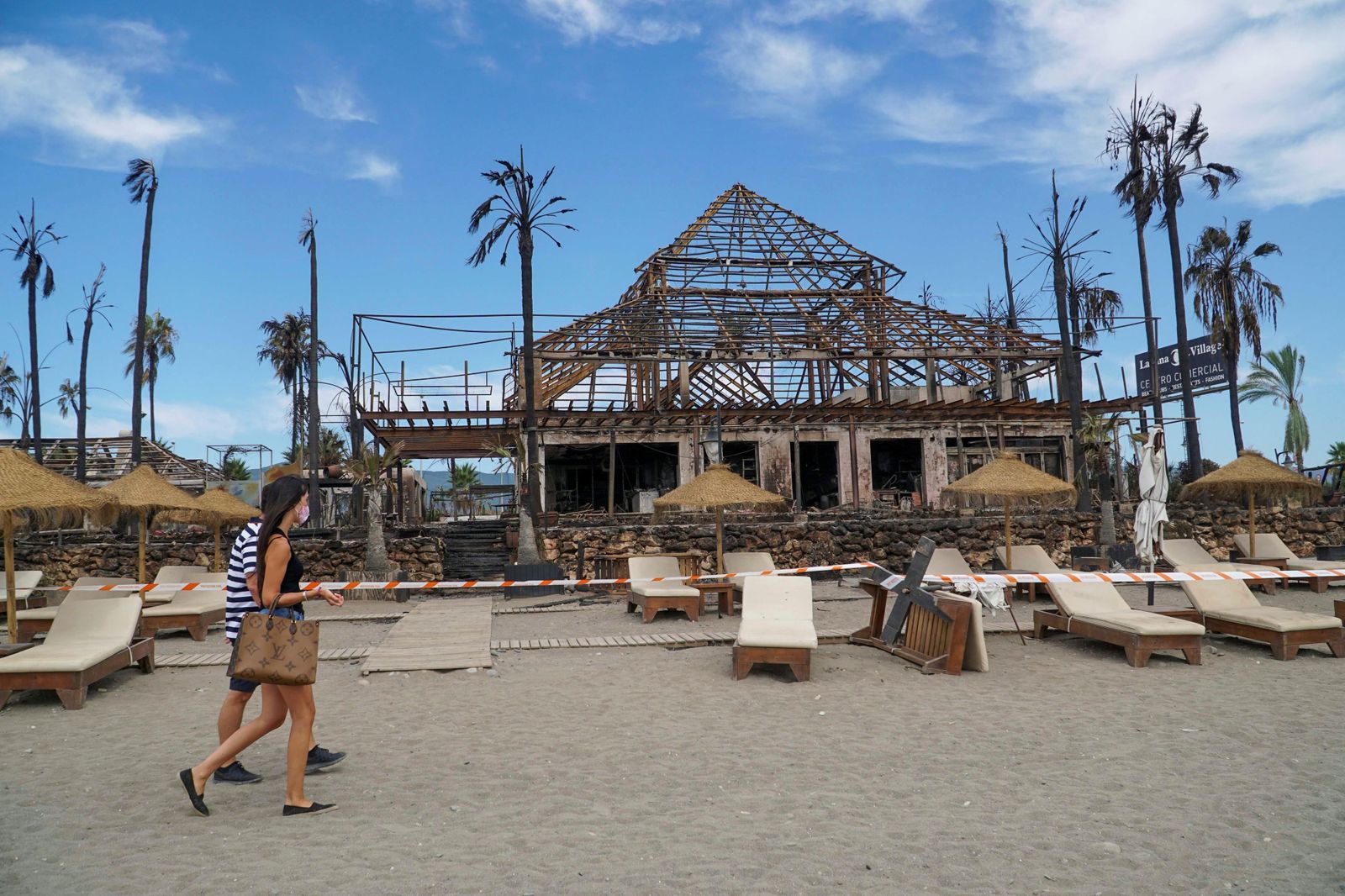 Dos personas pasan el domingo por delante del centro comercial calcinado.