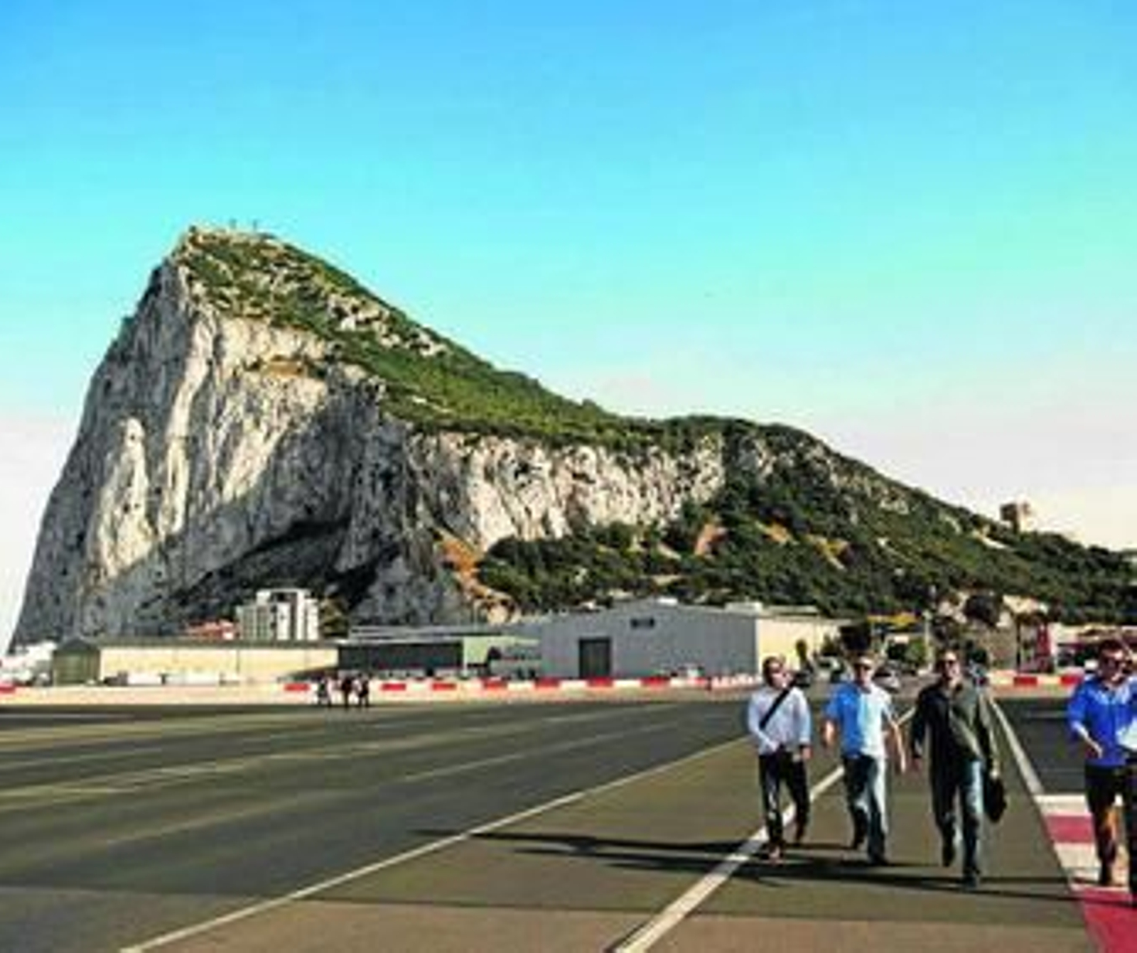 Varias personas transitan por el campo de aviación, con el Peñón al fondo.