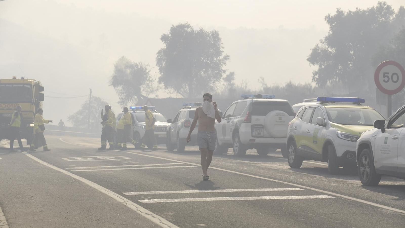 Una persona se tapa la cara con la camiseta para no respirar el humo del incendio