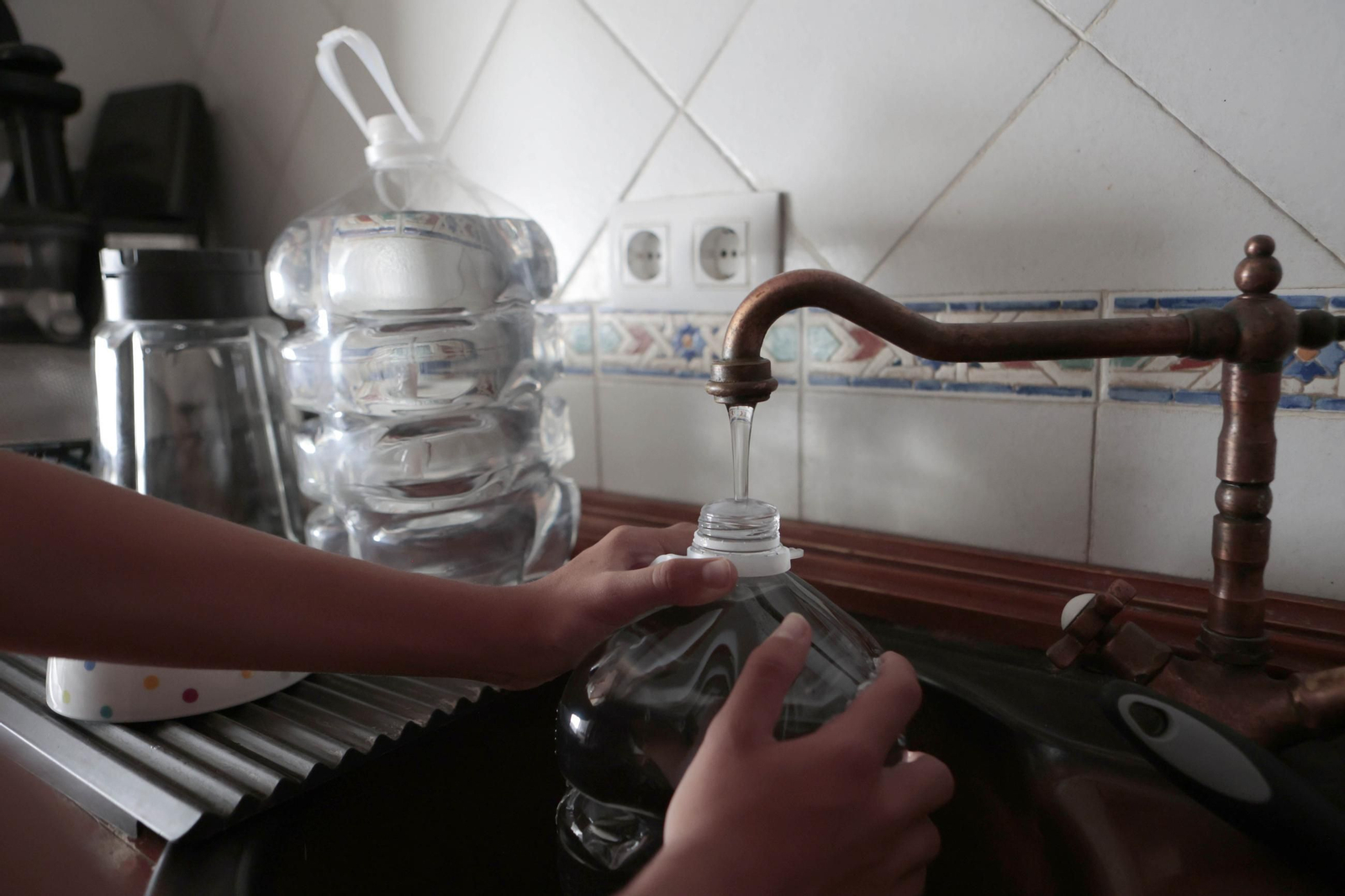 Una persona llena varias garrafas de agua en su vivienda.