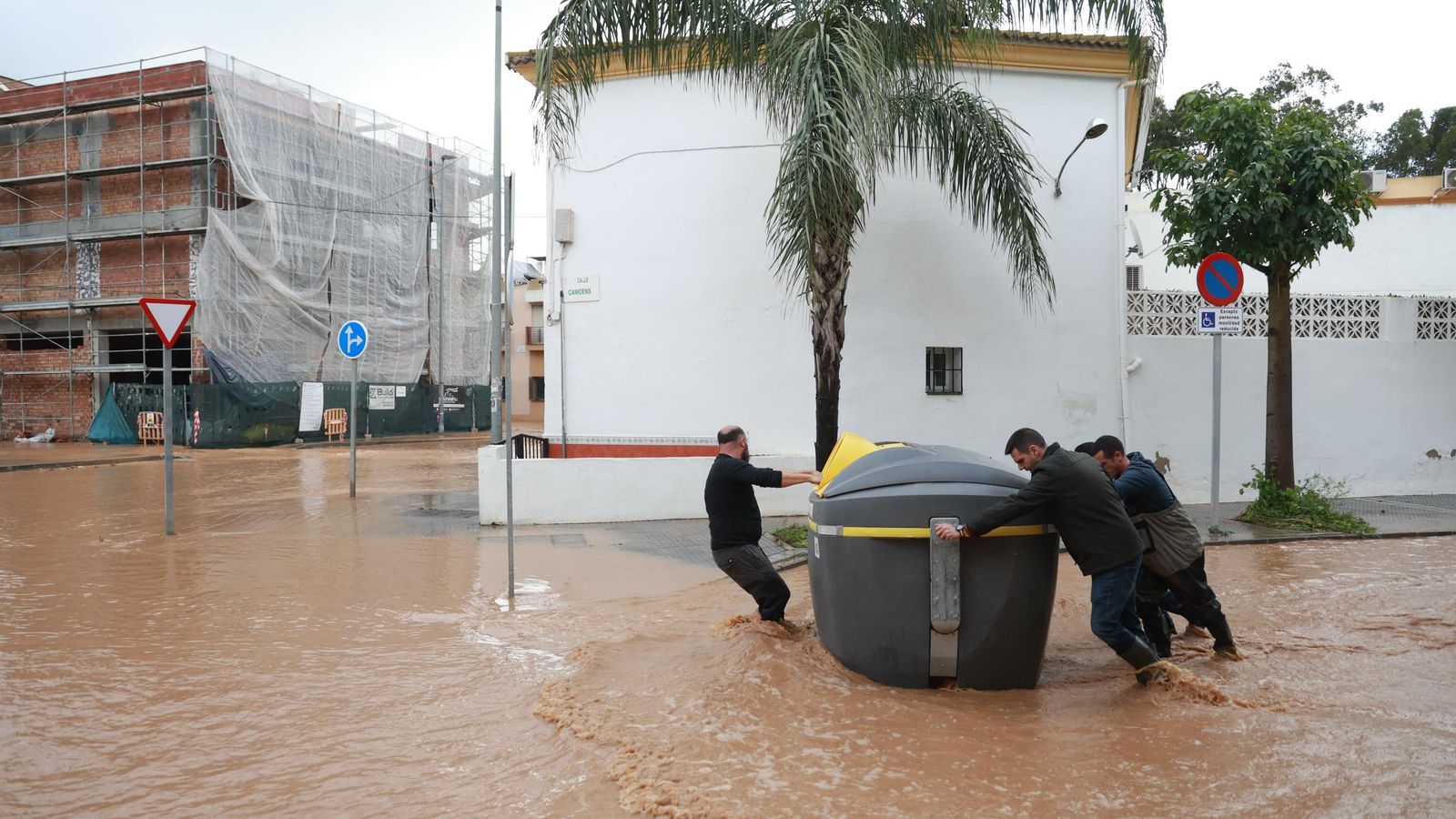 Vecinos empujan un contenedor arrastrado por la corriente para devolverlo a su sitio. 