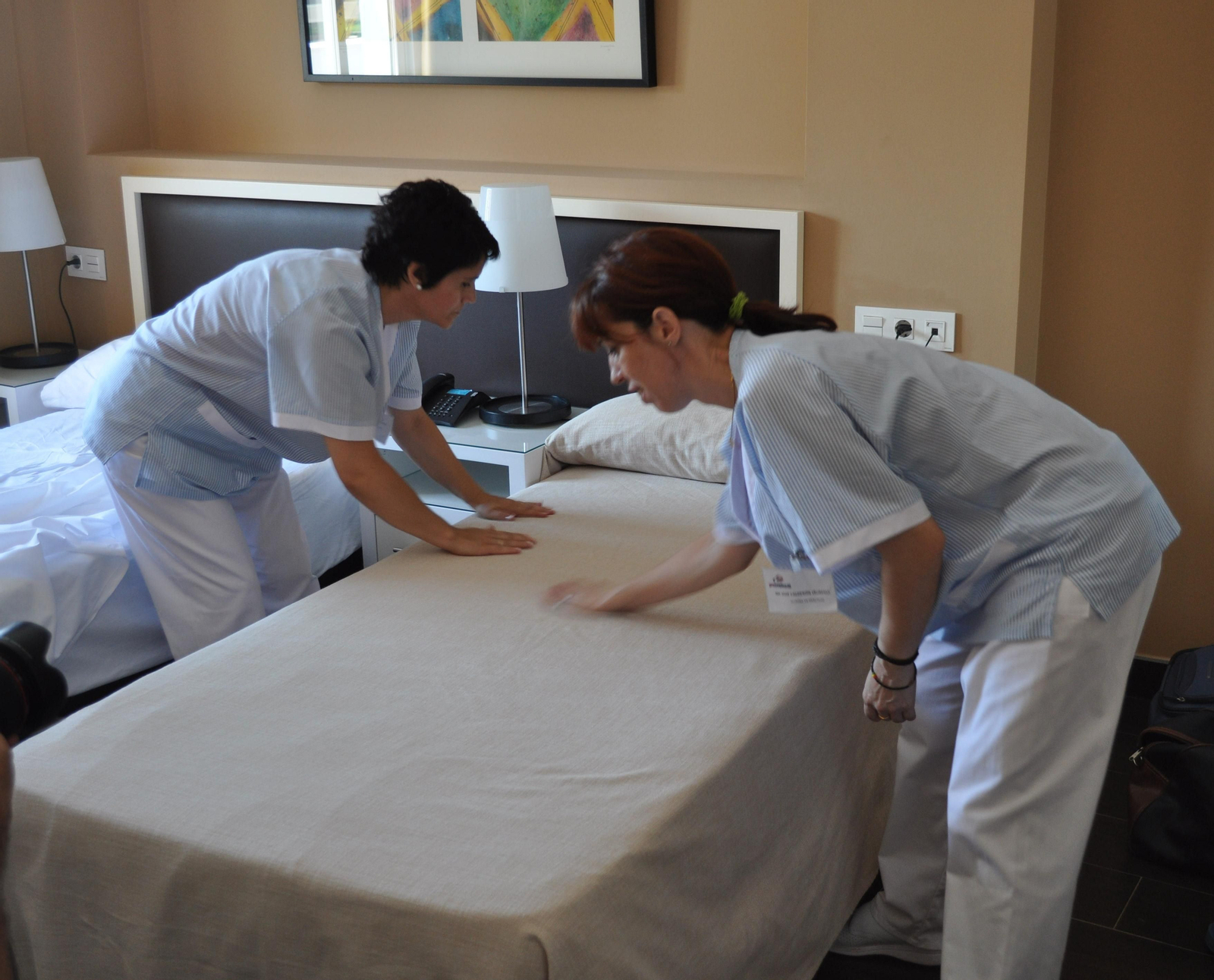 Dos mujeres hacen la cama de la habitación de  un hotel.