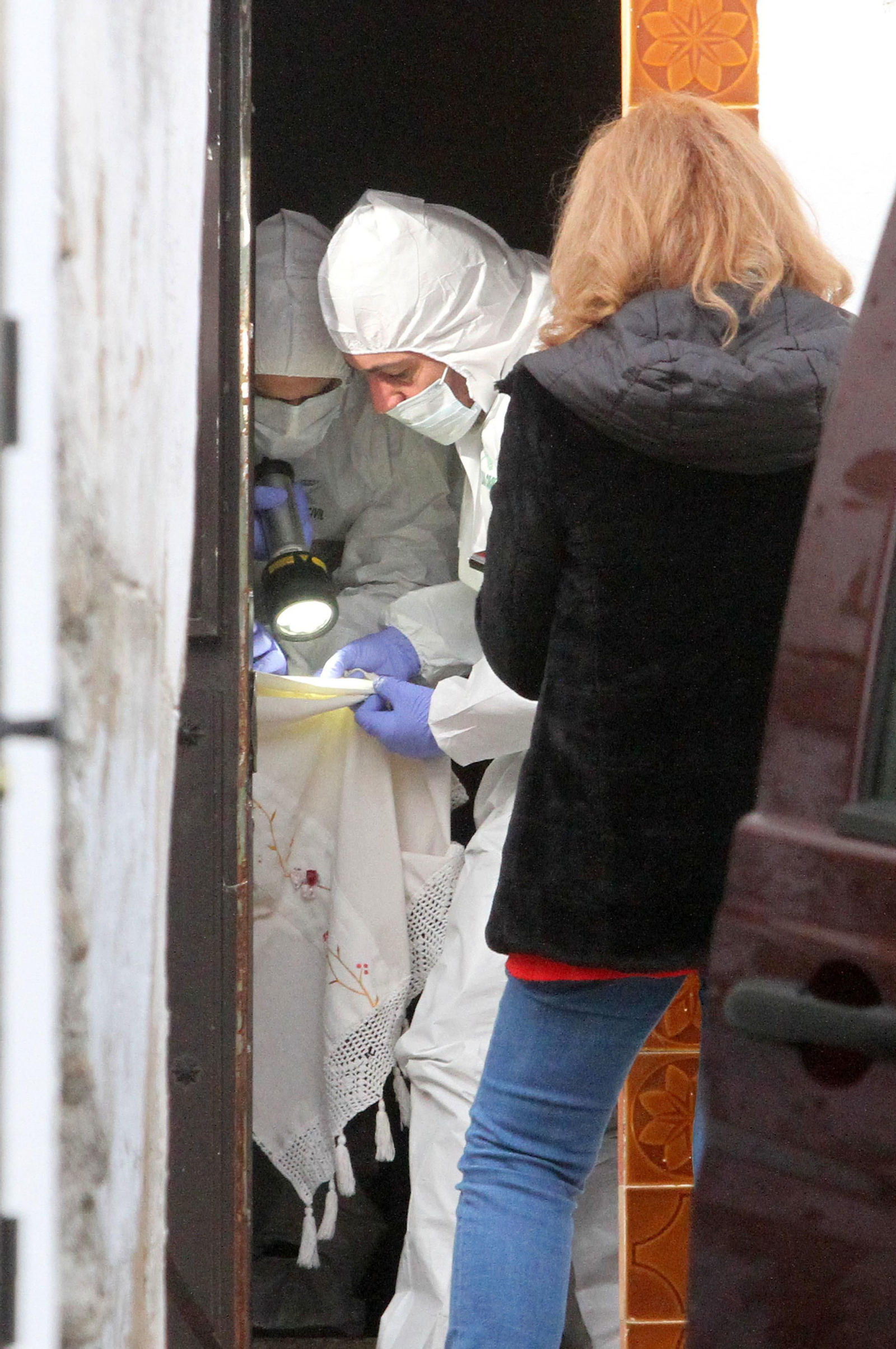 Dos efectivos del ECIO apuntan con una linterna a una sección de la cortina de la puerta de la casa del detenido.