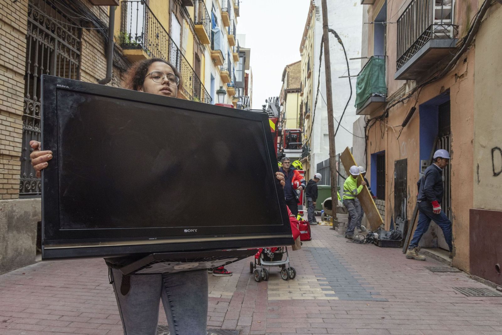 Una mujer abandona su vivienda con una televisión en brazos tras verse obligada a marcharse, una escena que refleja el impacto cotidiano de la ocupación y el desalojo en los barrios de Almería.
