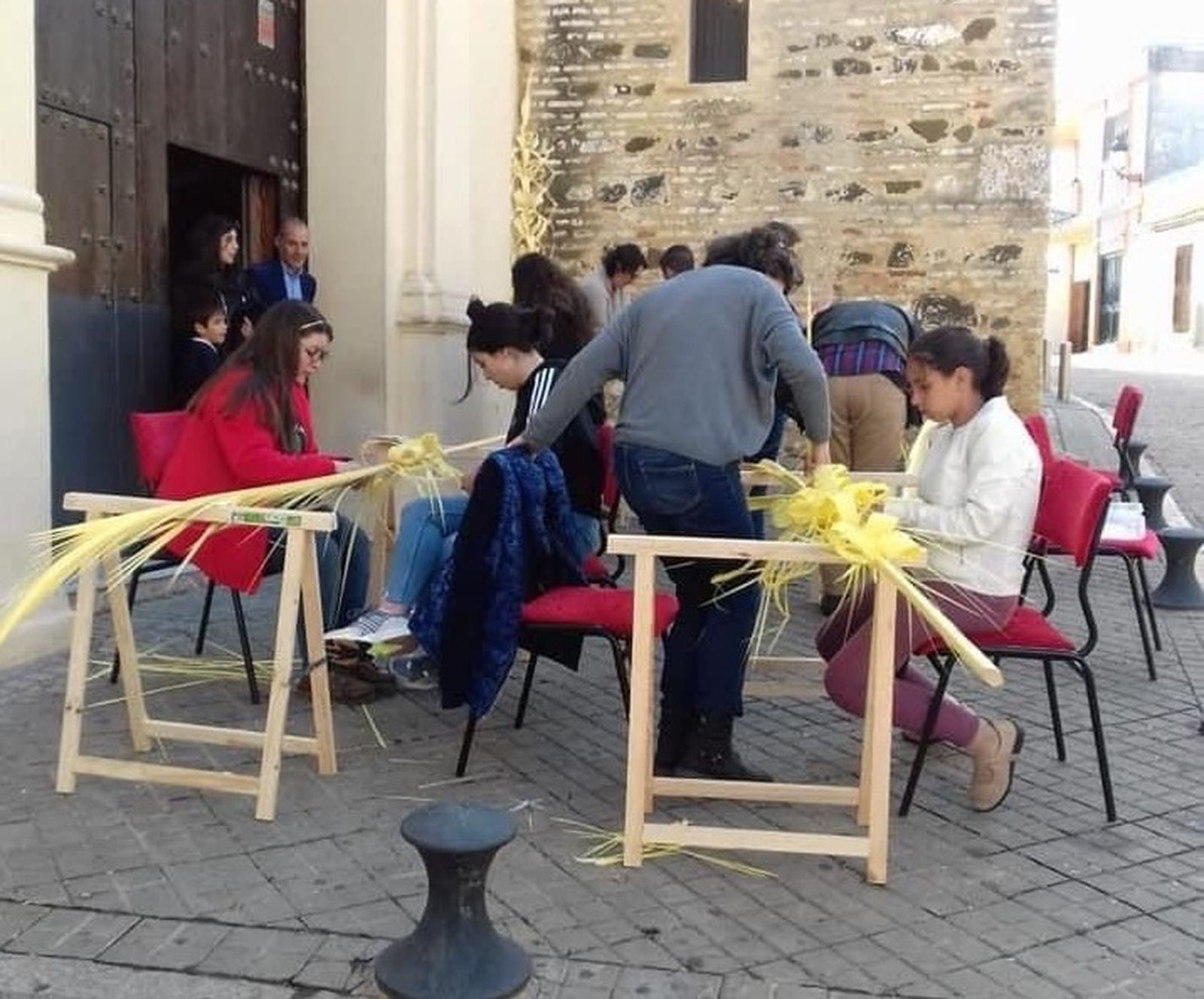 El grupo de rizadoras de palma trabajando en la puerta de la parroquia de San Pedro.