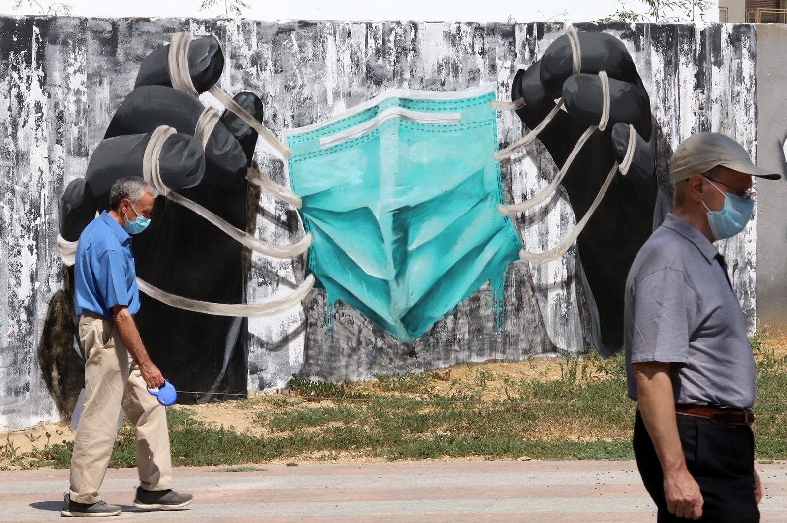 Un grafiti recoge unas grandes manos sujetando una mascarilla.