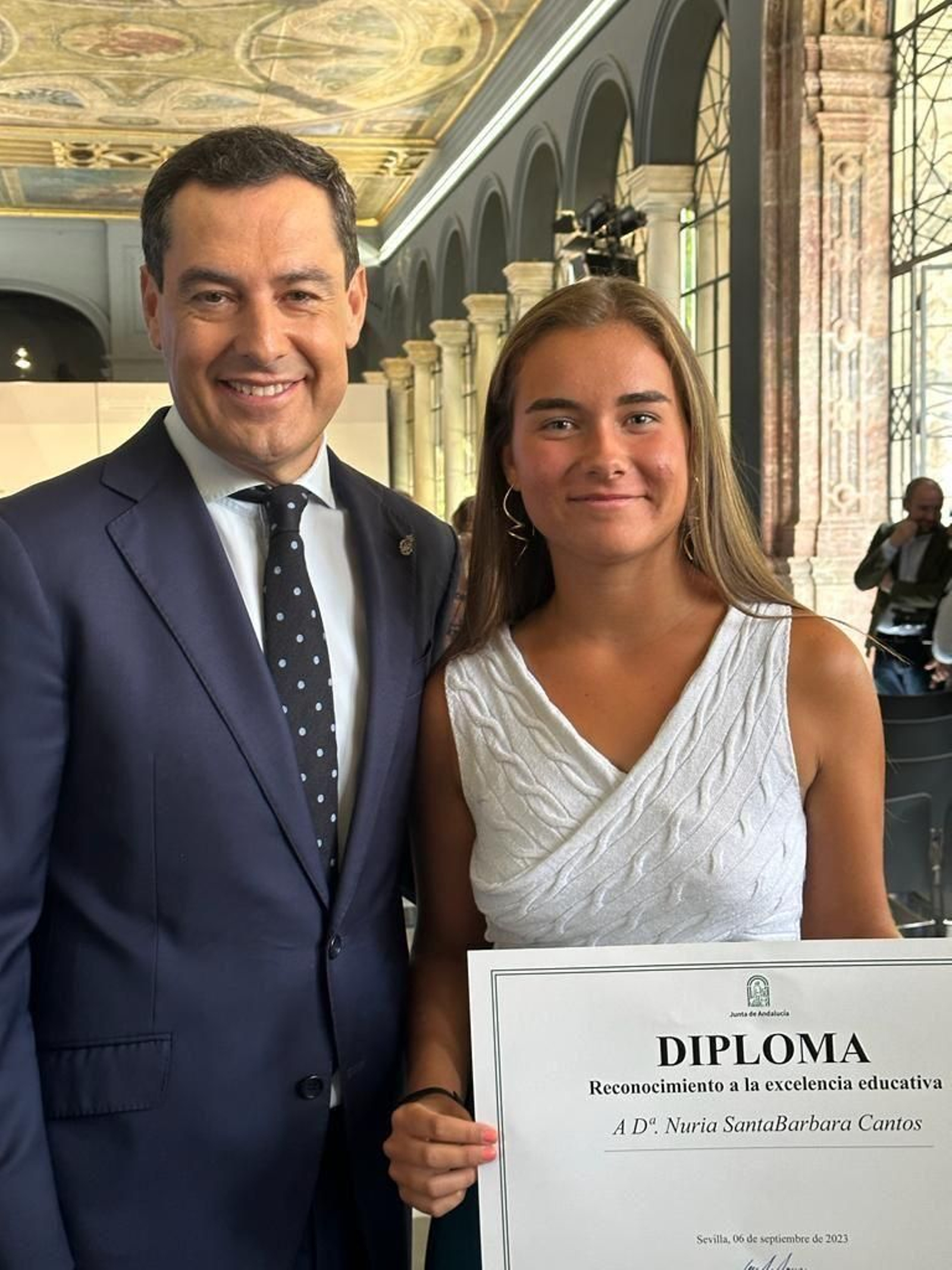 La isleña Nuria Santabárbara posa con el presidente de la Junta de Andalucía tras recibir el reconocimiento a la excelencia educativa por su expediente de Bachillerato.