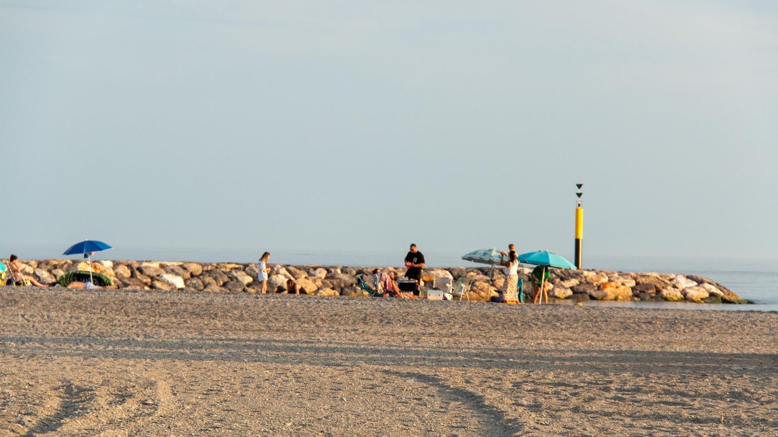 Varias personas disfrutan del día de playa junto al espigón de Motril