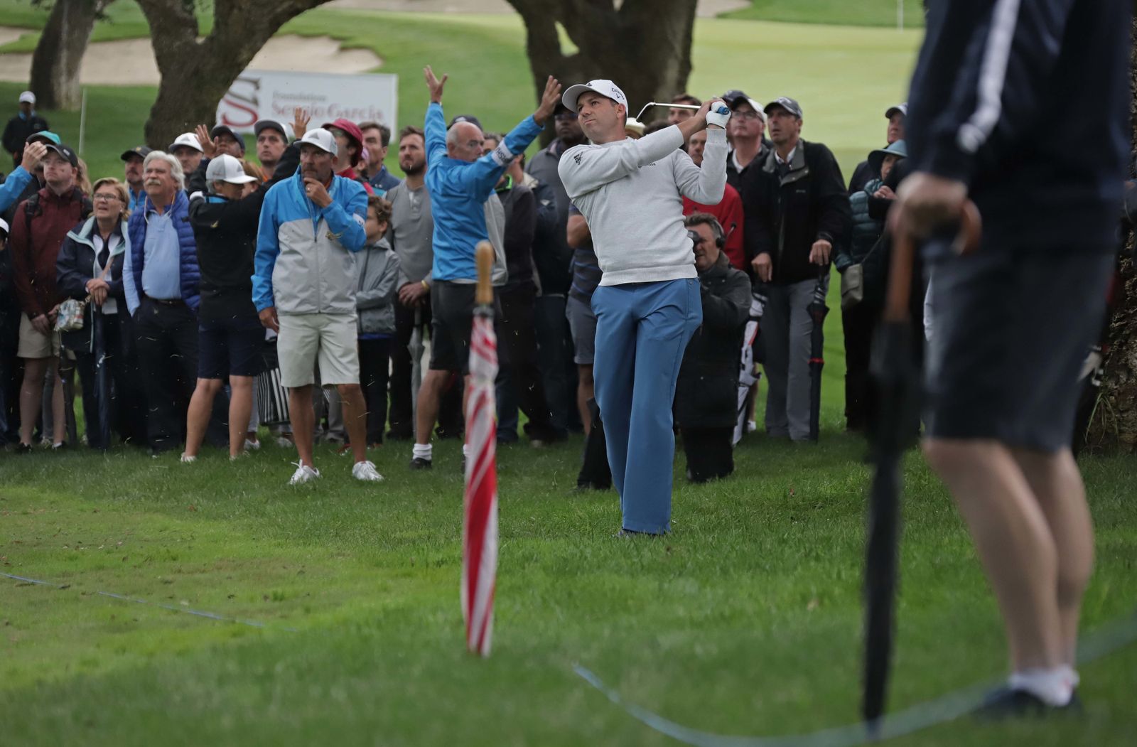 Sergio García golpea la bola, con un paraguas clavado en el césped en primer término