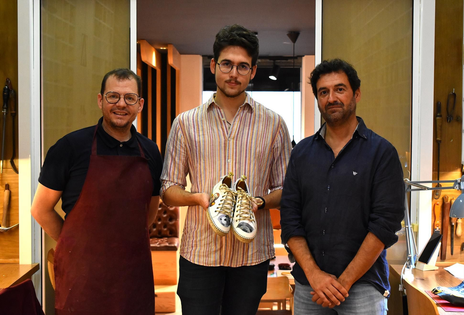 Abraham Zambrana (i), Cristian Álvarez (c) y Manuel Romero Bejarano posan con los zapatos en la tienda-taller de Zambrana, en Jerez.