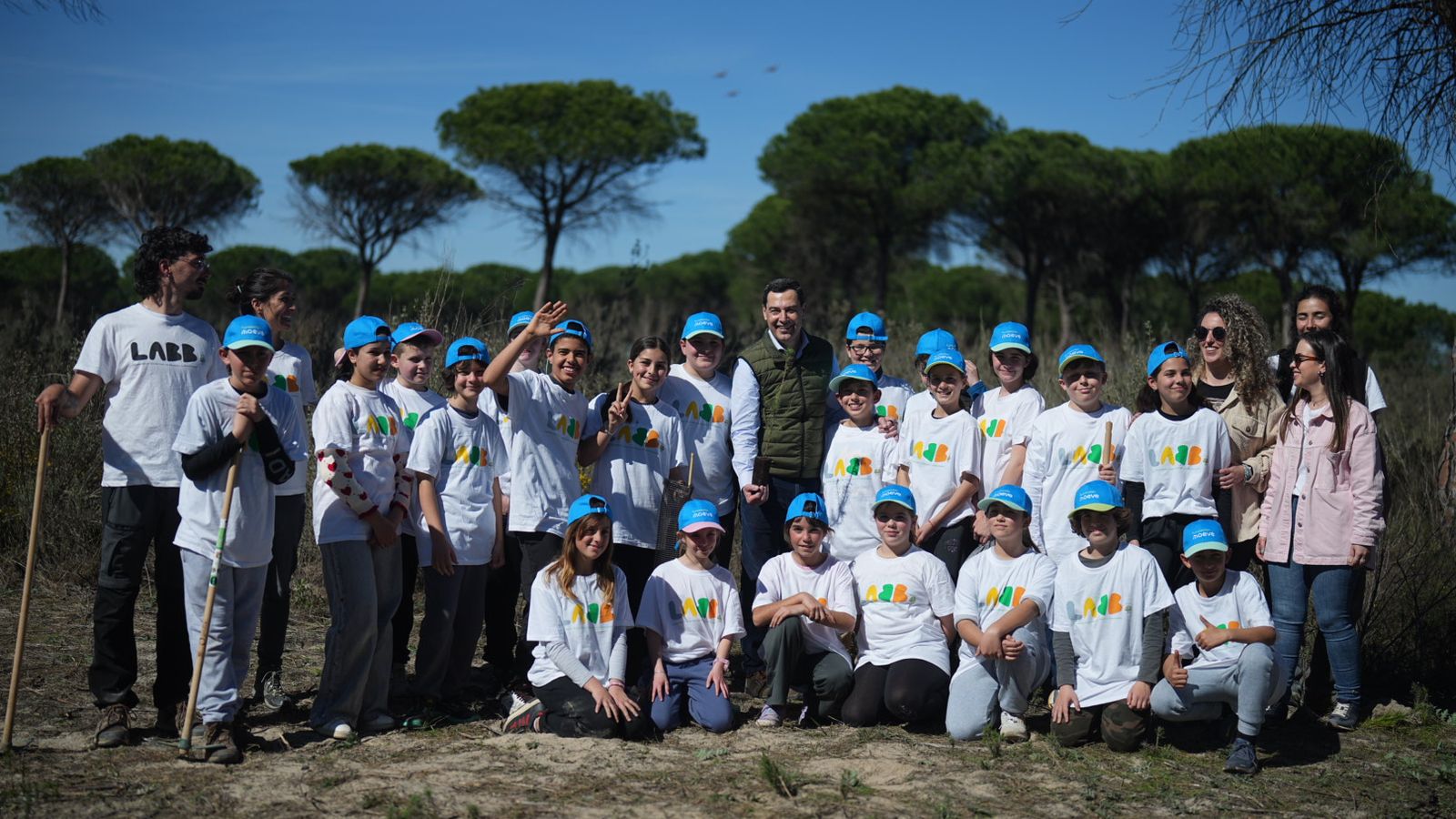 Juanma Moreno con los jóvenes que participan en una plantación de árboles en el paraje de 'Las Peñuelas', dentro del Espacio Natural de Doñana..