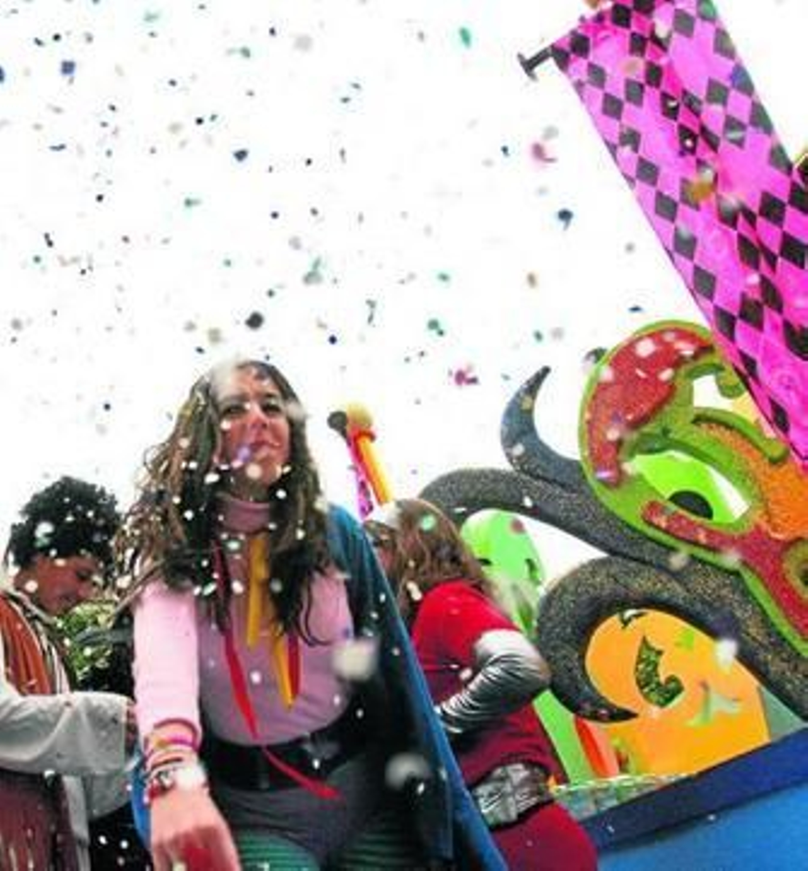 Una joven montada en una carroza arroja confeti hacia el público asistente.