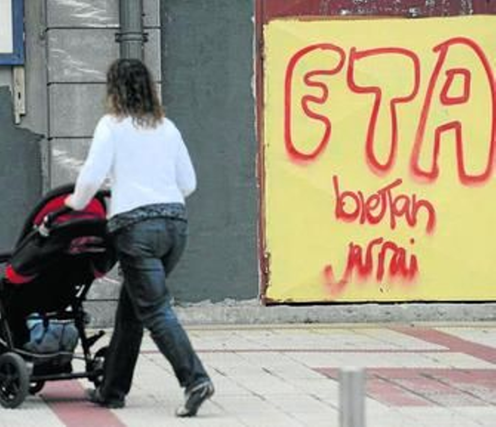 Una mujer pasea a su carrito delante de una pintada en favor de ETA.