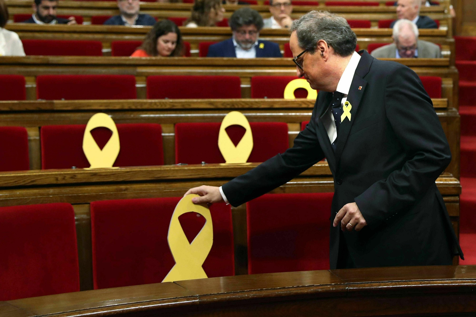 El presidente de la Generalitat, Quim Torra, coloca un lazo amarillo en un pleno del Parlamento catalán.
