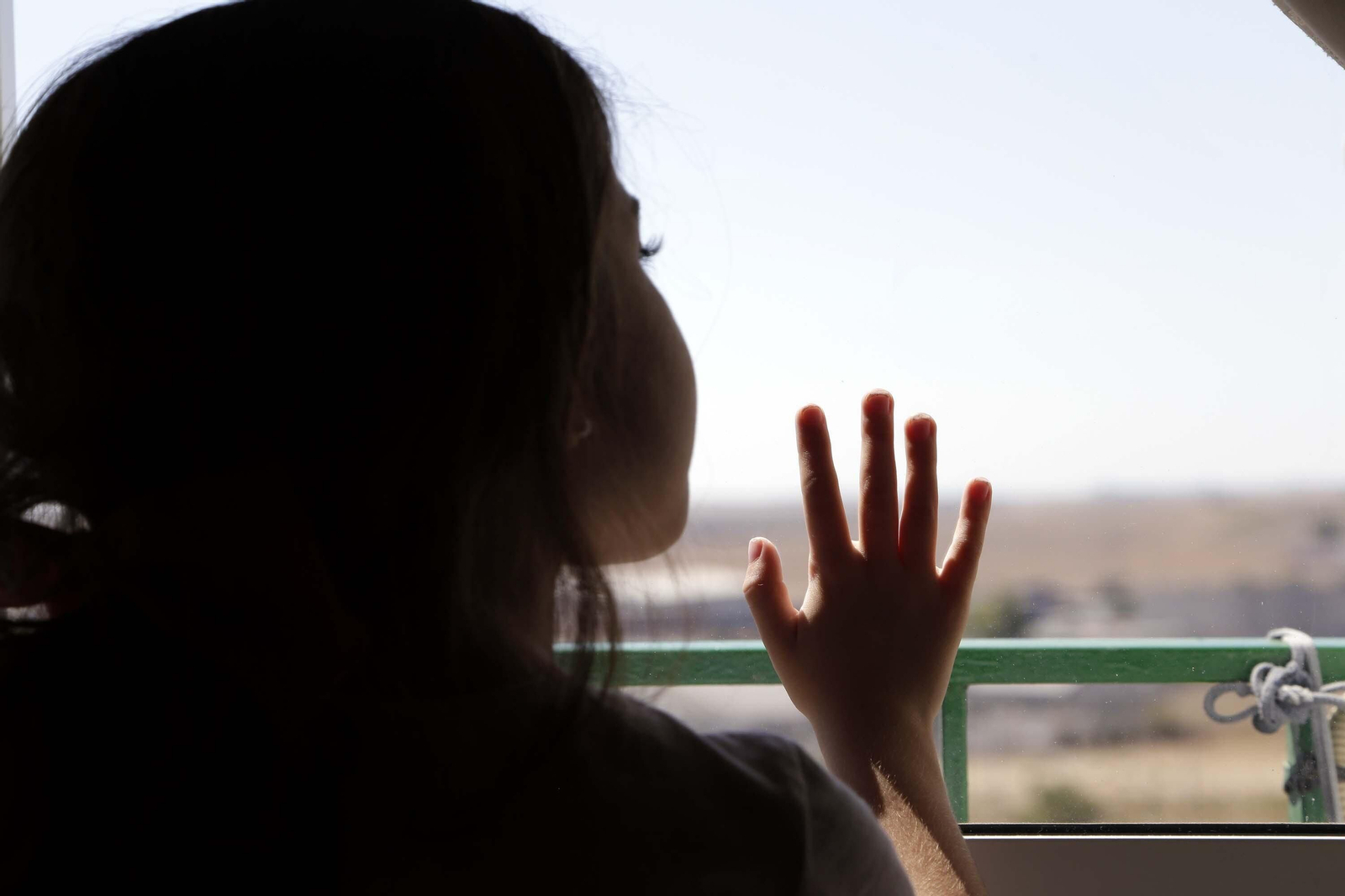Una niña asomándose por una ventana.