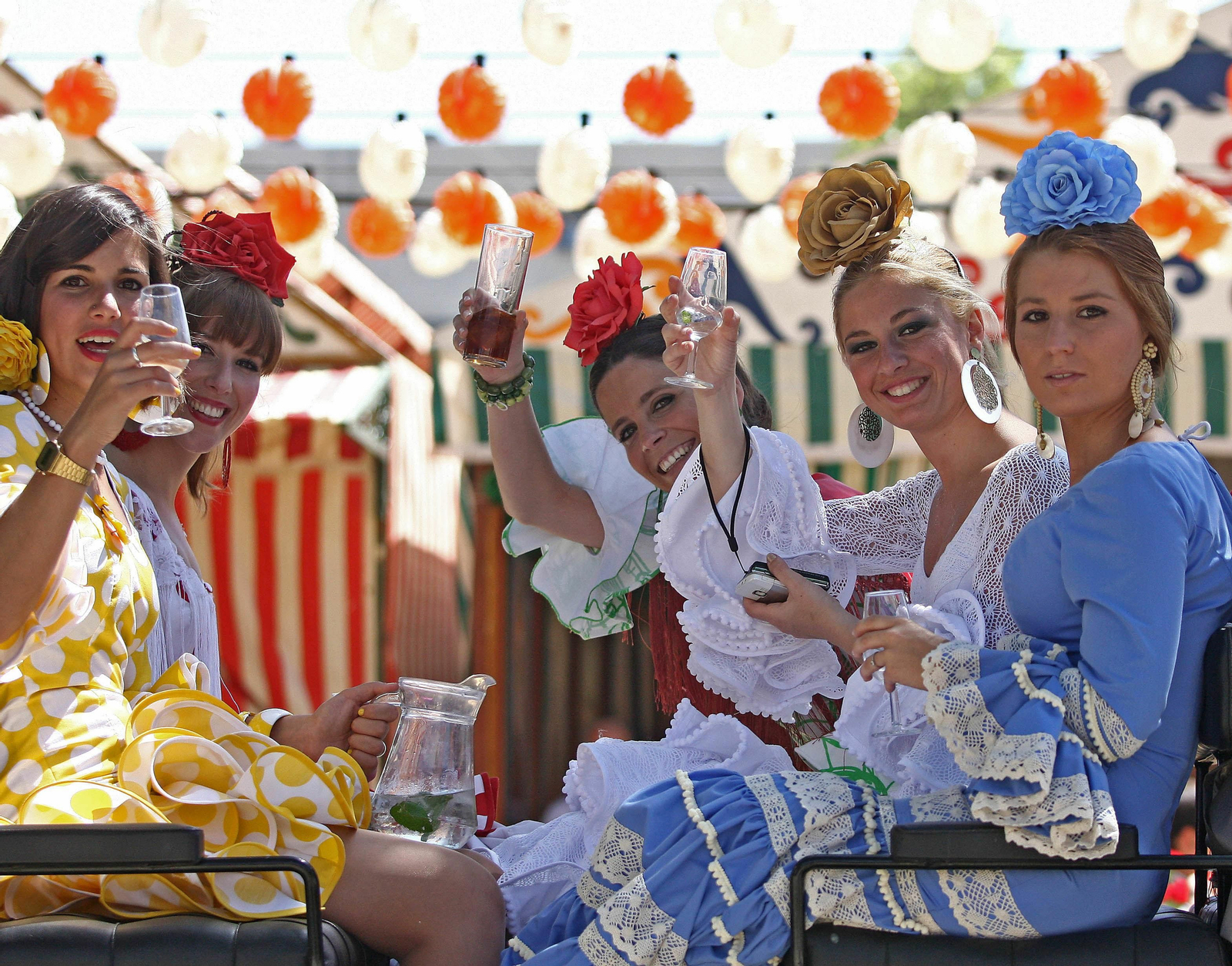 Mujeres vestidas de flamenca en un coche de caballos, bebiendo rebujito.