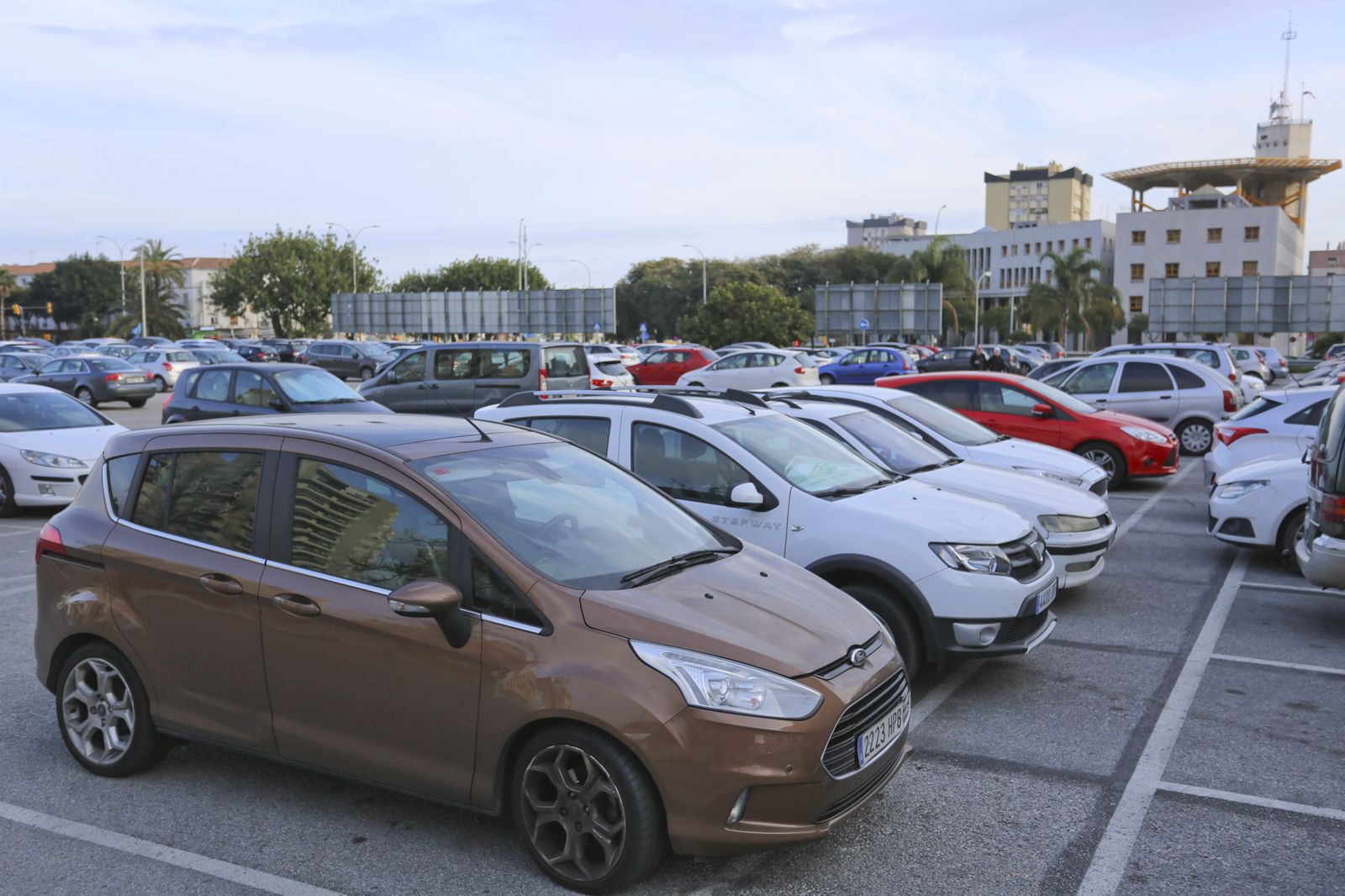 Decenas de coches aparcados en la parcela y al fondo, la Comisaría provincial de la Policía Nacional.