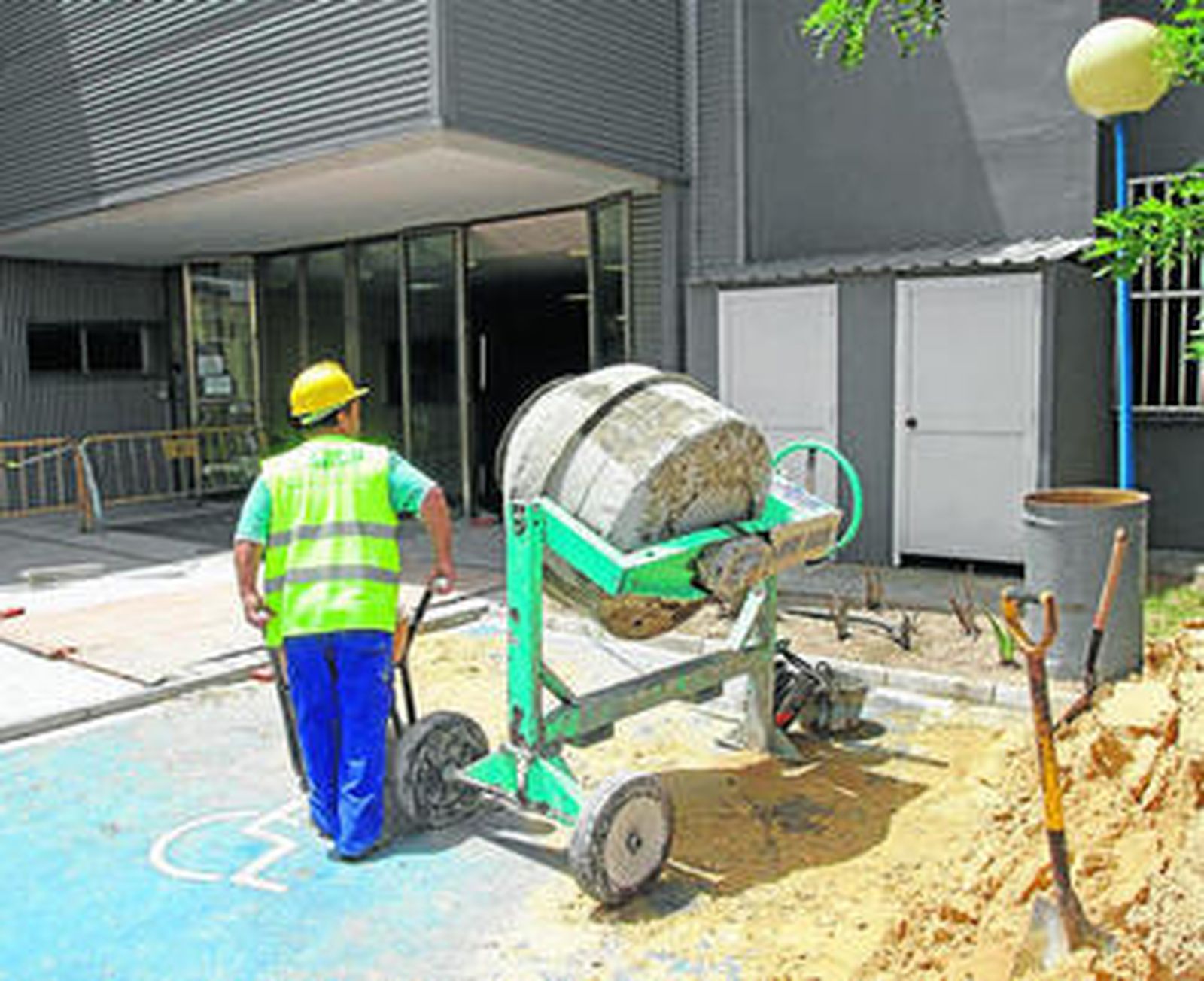 Un operario maneja una carretilla junto a la hormigonera en el exterior del edificio.