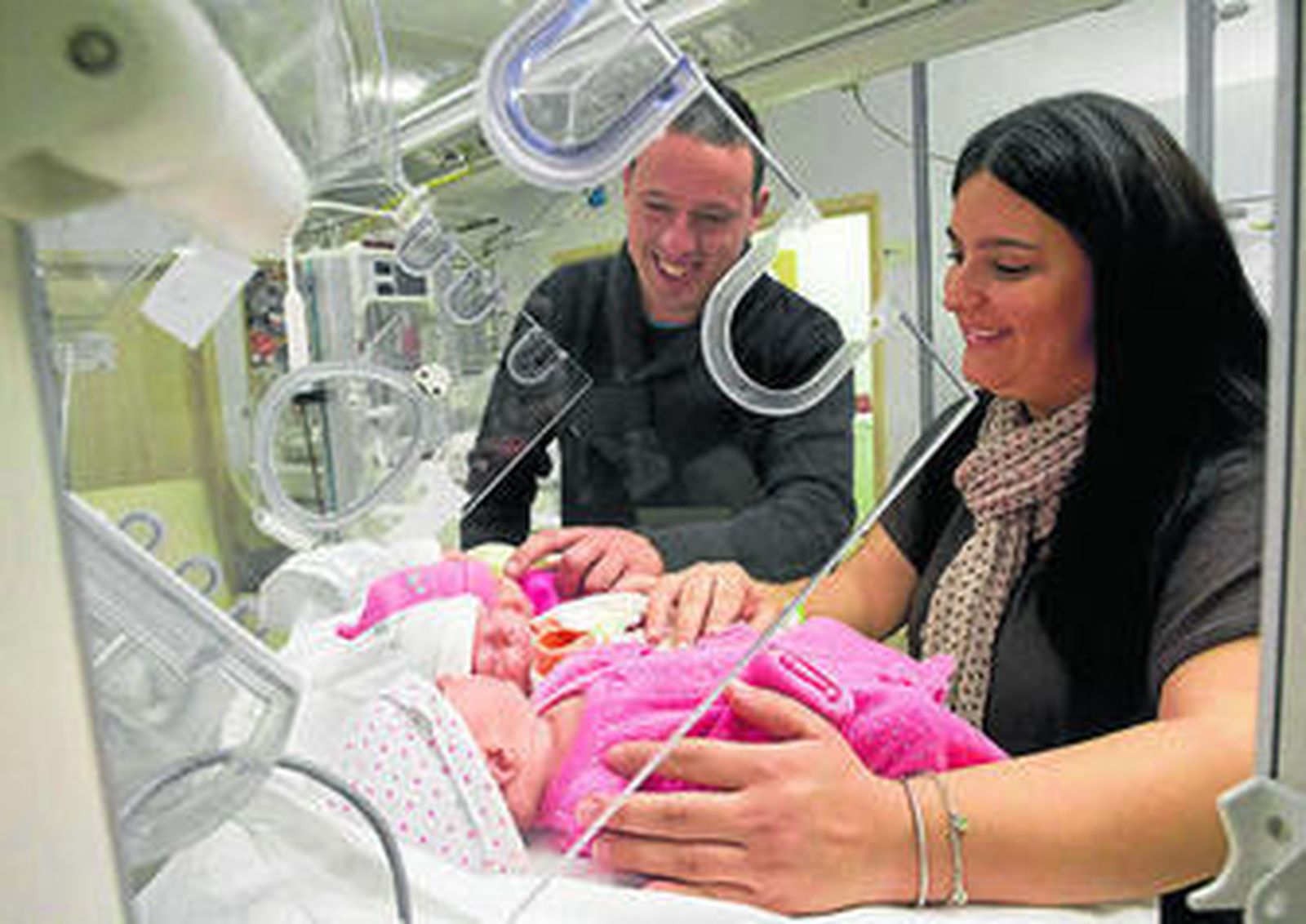 Los padres observan a sus cuatro hijos que descansan en la incubadora.