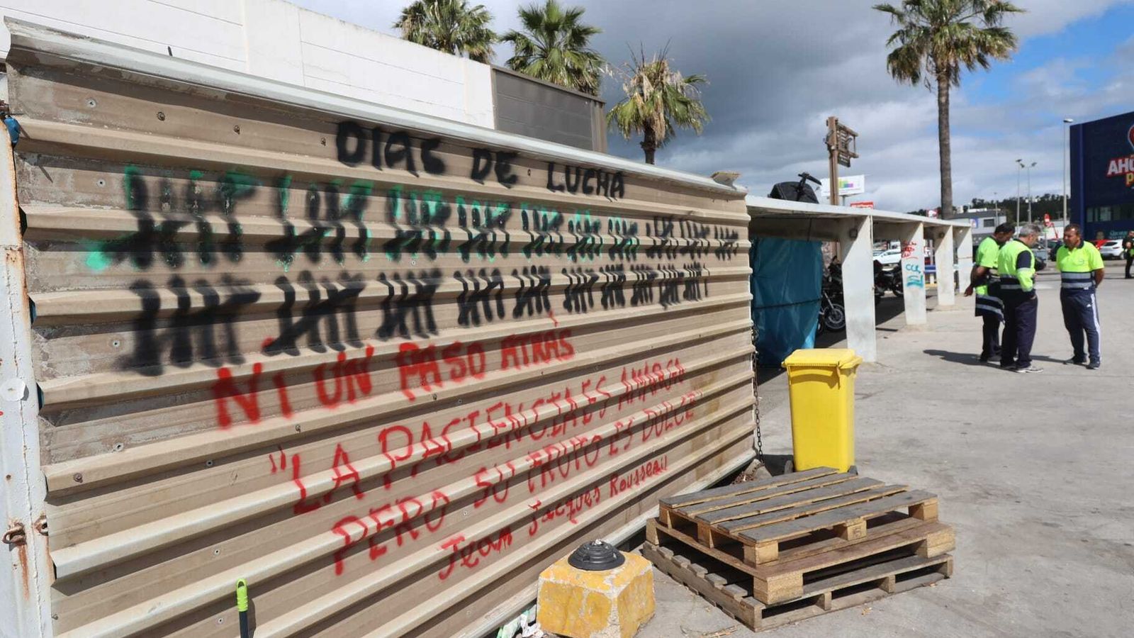 Una valla con pintadas y a lo lejos varios trabajadores de Acerinox.