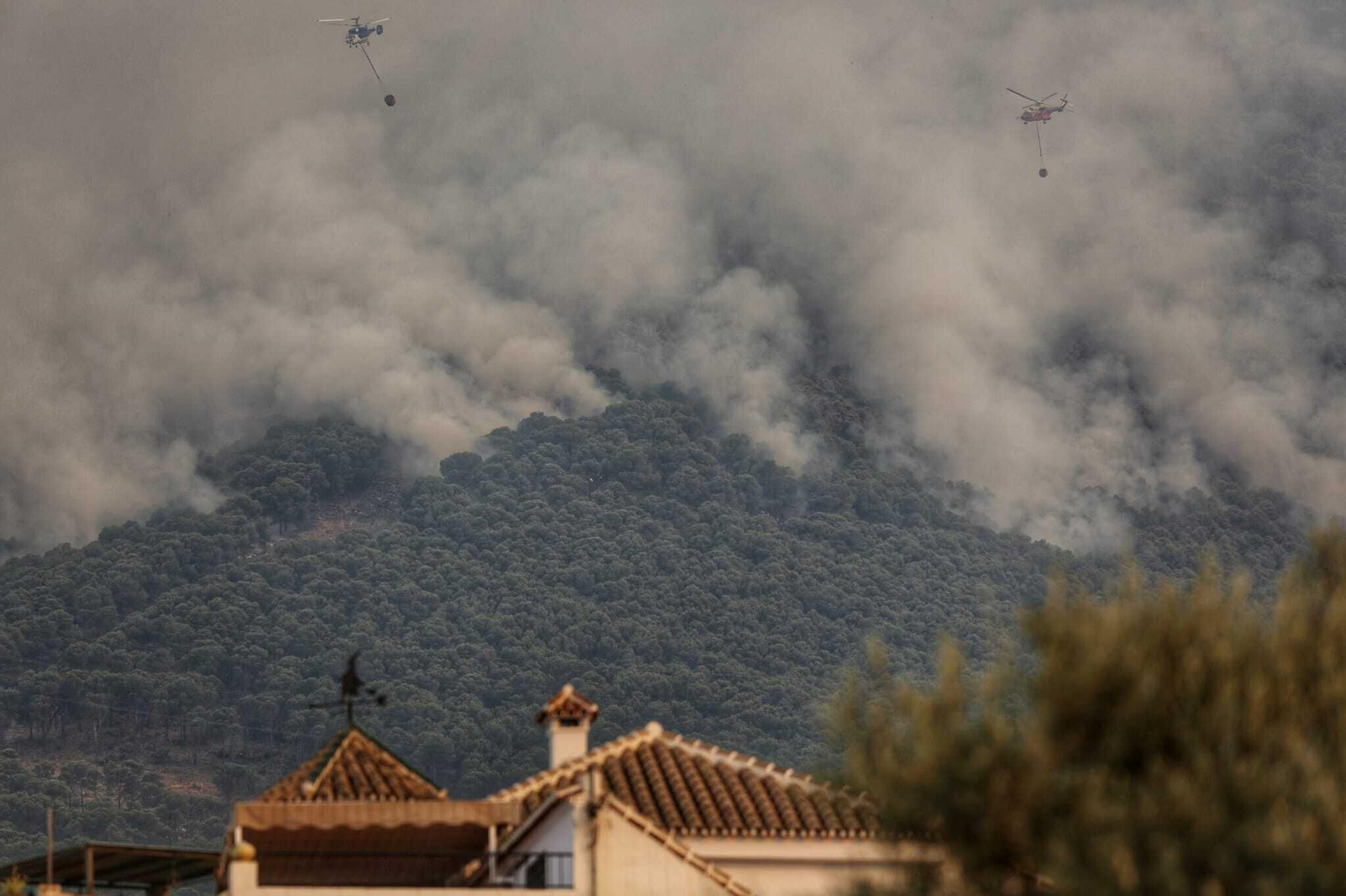 Dos helicópteros luchando contra el fuego, con la sierra de fondo.