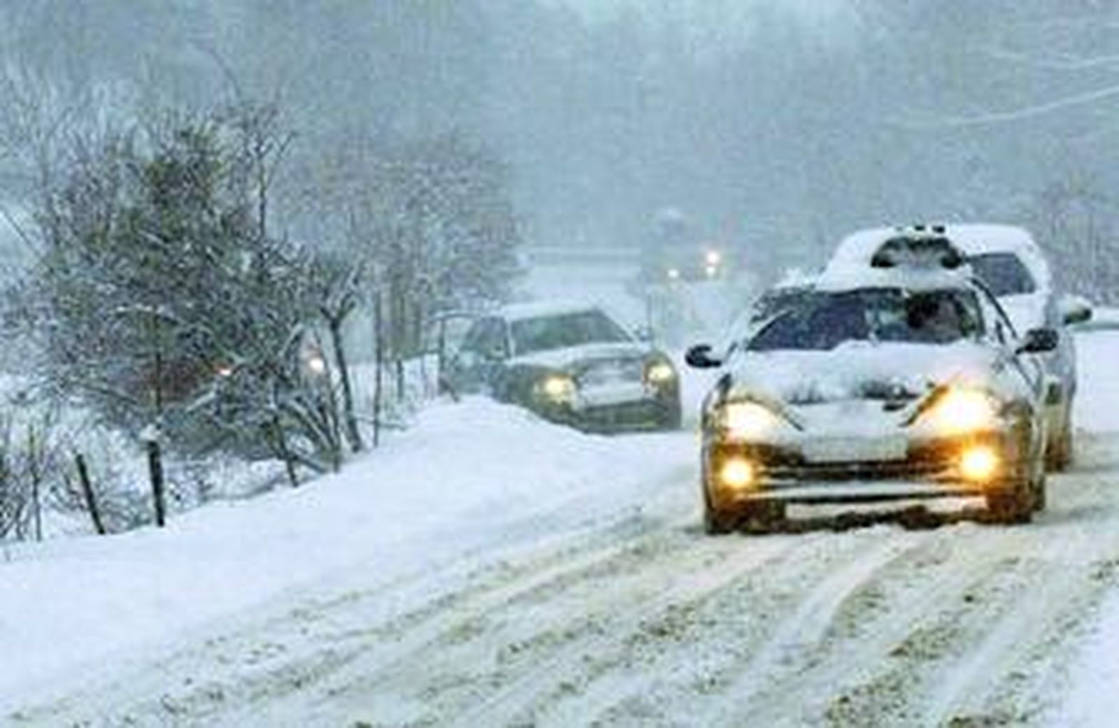 Varios vehículos circulan con precaución por una vía cubierta de nieve.