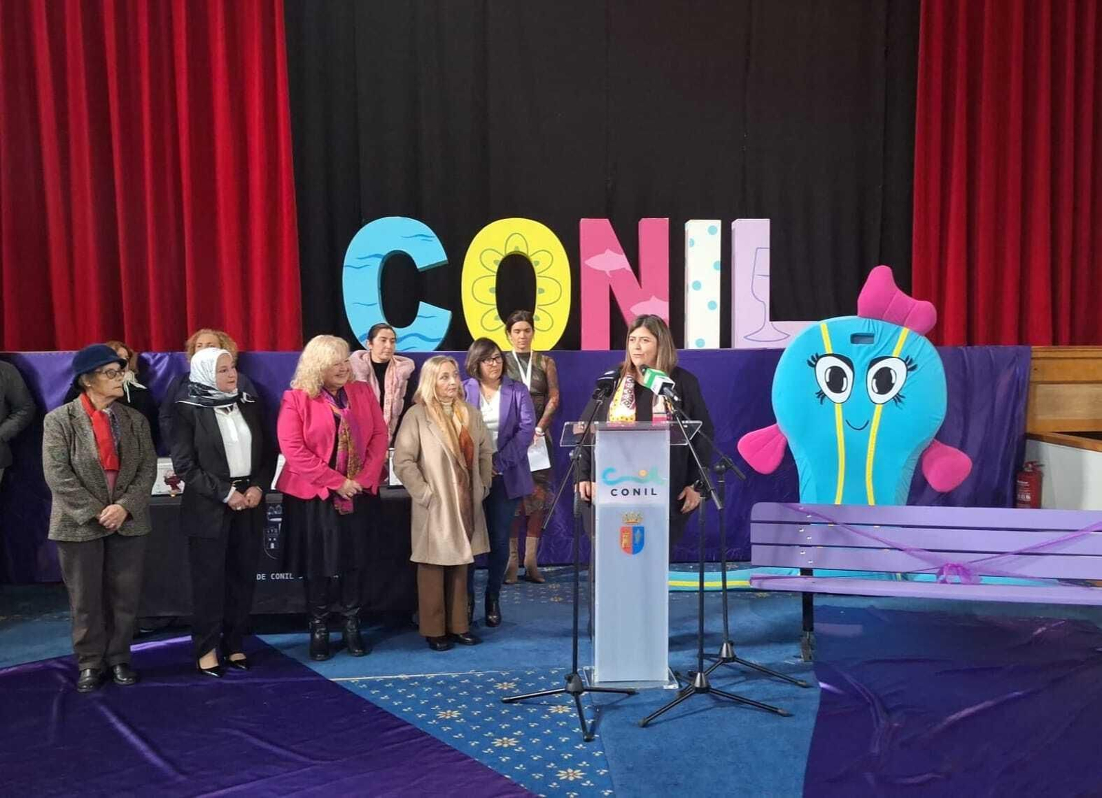 La alcaldesa junto a las cinco mujeres homenajeadas, la mascota 'Conilete' y el banco de la Igualdad.