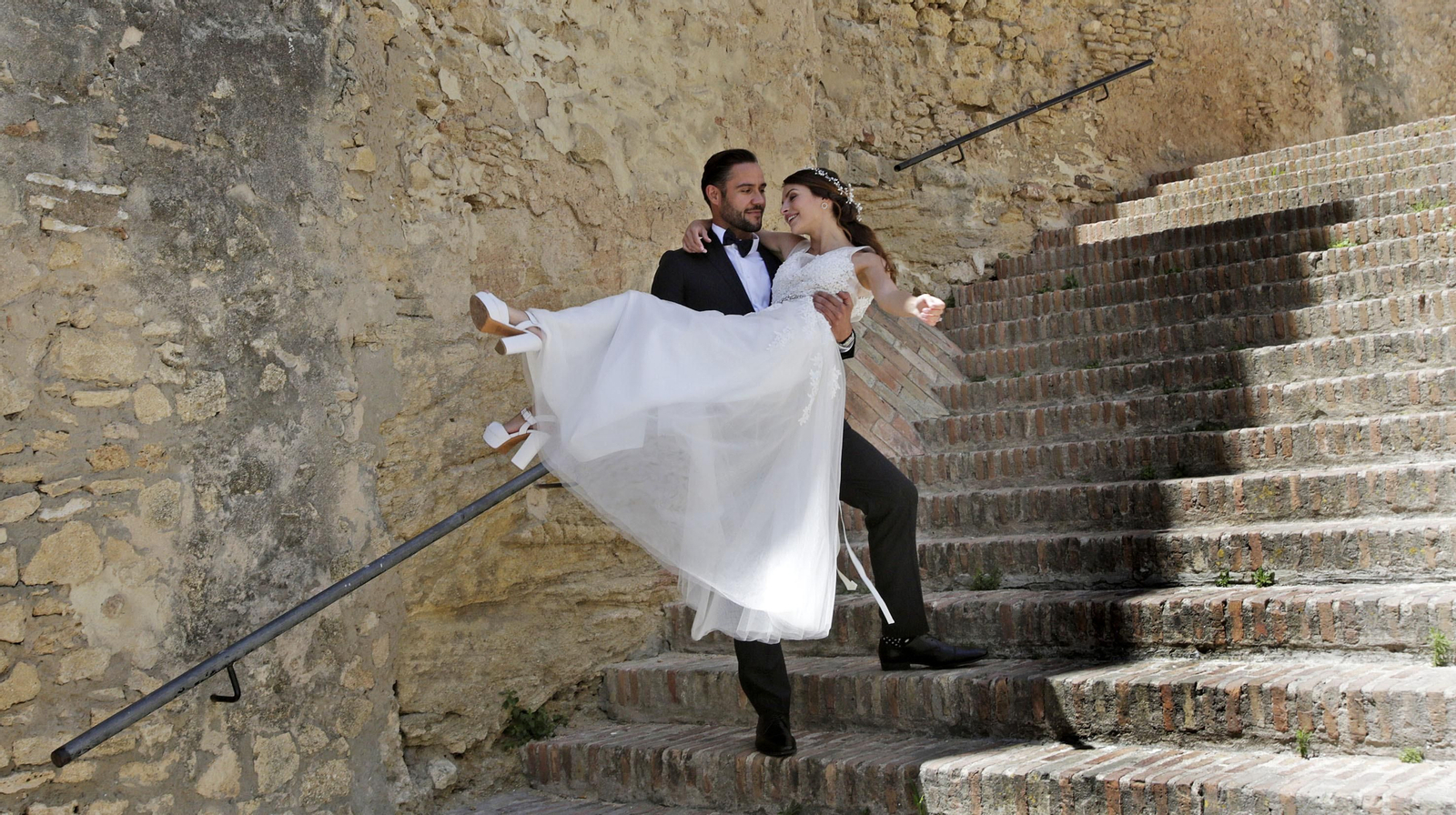 Una pareja vestida de novios baja por las escaleras de la muralla.