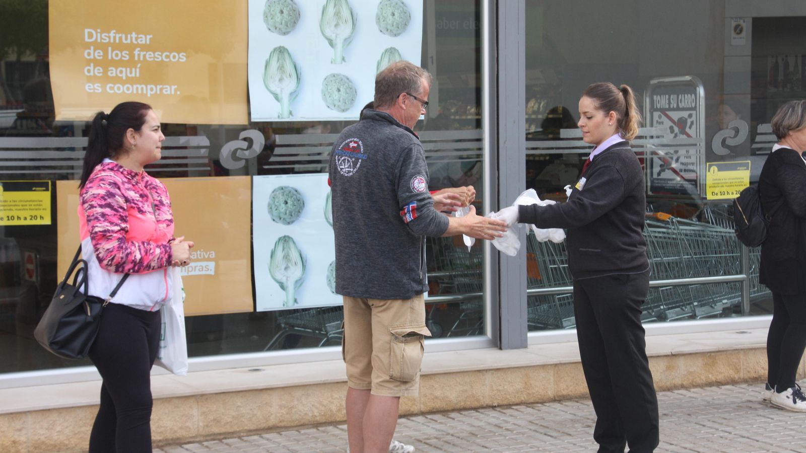 Una empleada de un supermercado proporciona gel y guantes a un cliente, a las puertas de la tienda.