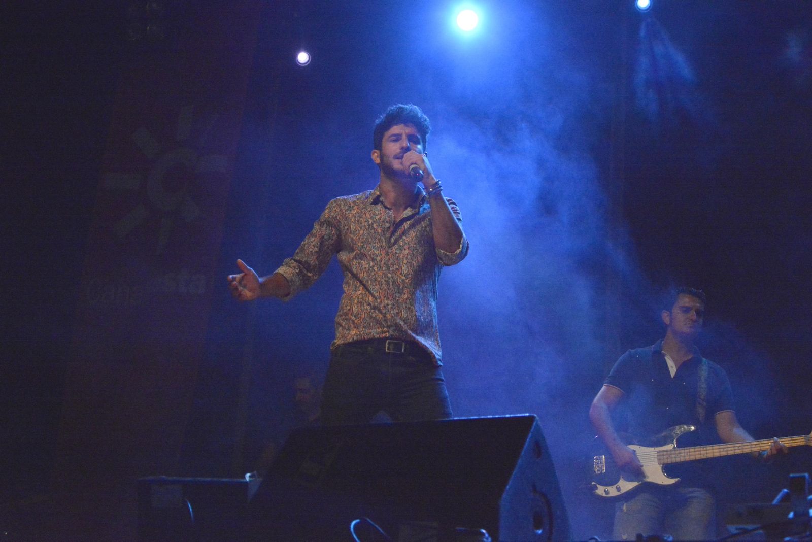 1. Carlos Torres, concursante de la última edición del programa La Voz.  2. El público asiste al concierto con artistas como Lérica o Maíta Vende Cá.  3. Un gran número de personas camina por una calle del ferial. 4. Un niño observa uno de los puestos de la feria. 5. Varias personas en una tómbola. 6. Una de las casetas repletas de gente durante la noche. 7. Aglomeración de gente en la calle de las atracciones.