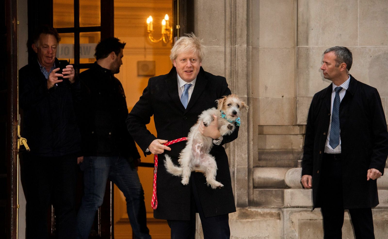 Boris Johnson sale de un centro de votación con su perro en brazos.