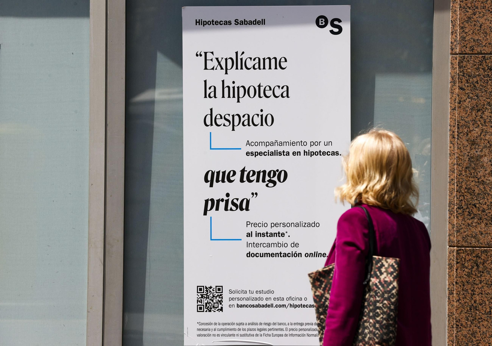 Una mujer observando un cartel de Sabadell sobre hipotecas