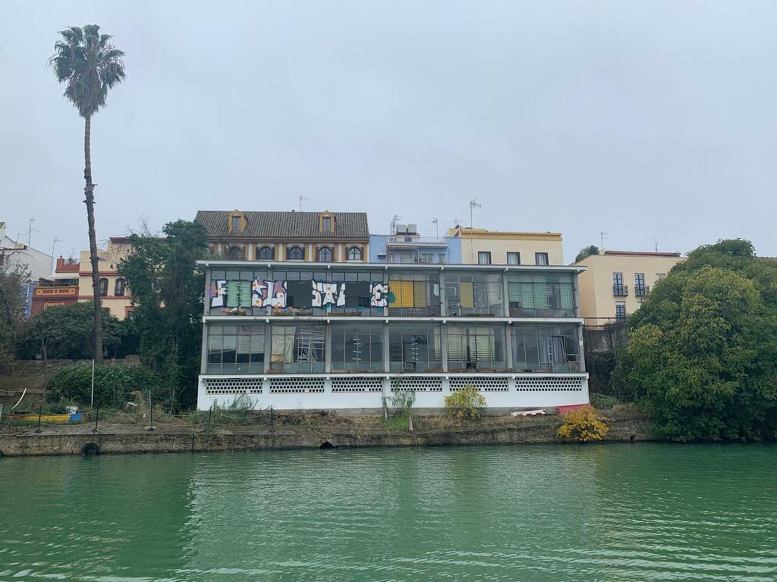 Cristales y persianas rotas y pintadas en la fachada del edificio que mira hacia el río, frente al centro de recepción de visitantes.