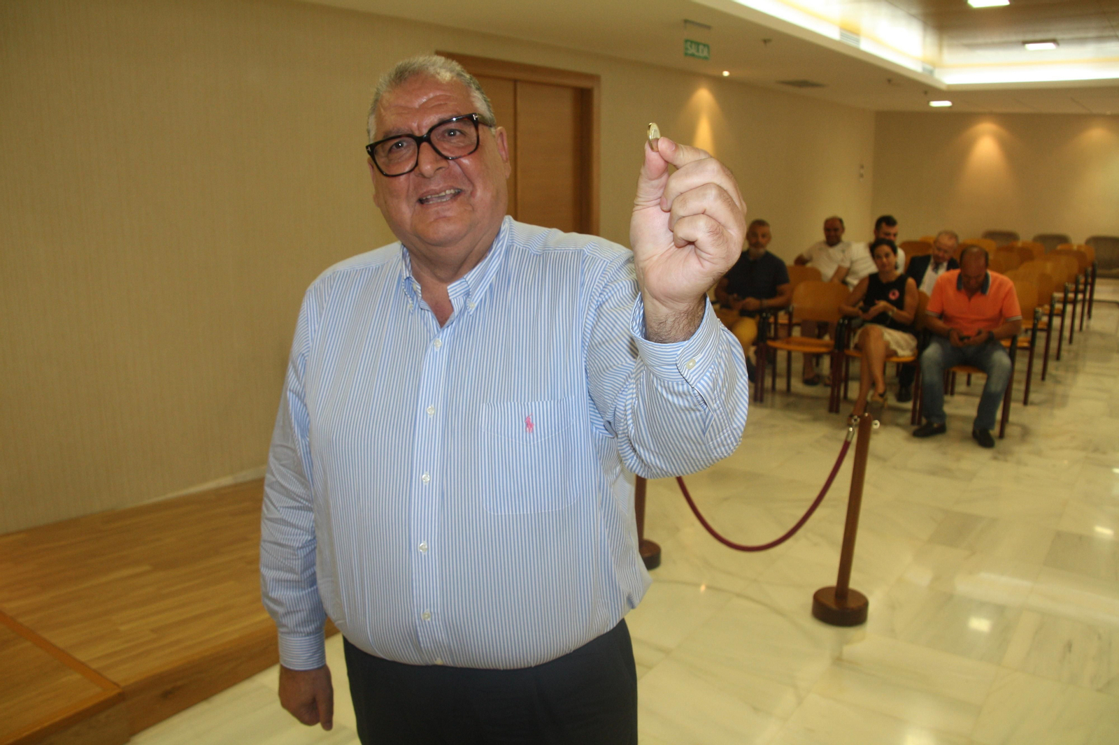 El secretario municipal muestra la moneda con la que realizó el sorteo durante el Pleno.