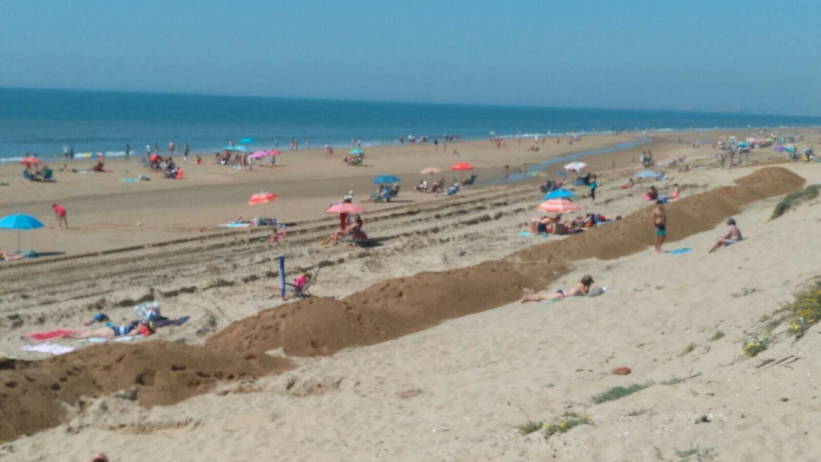 Bañistas de Islantilla entre un largo montículo de arena. En el recuadro, una máquina en la playa el miércoles.